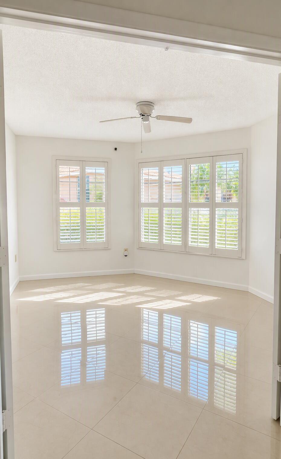 Interior space featuring large-format tile flooring, plantation shutters, and a ceiling fan