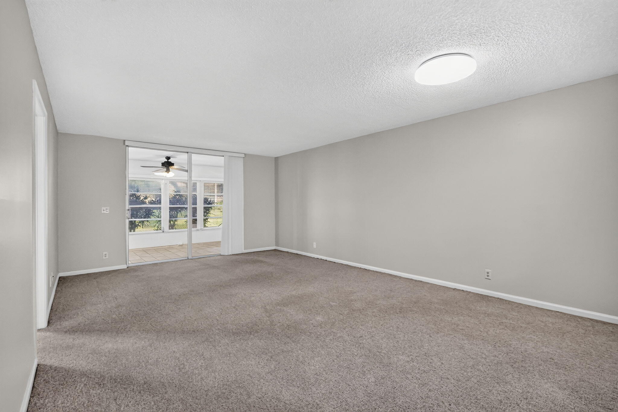 Neutral-toned interior space featuring wall-to-wall carpeting, a flush-mount ceiling light fixture, and a sliding glass door providing external access