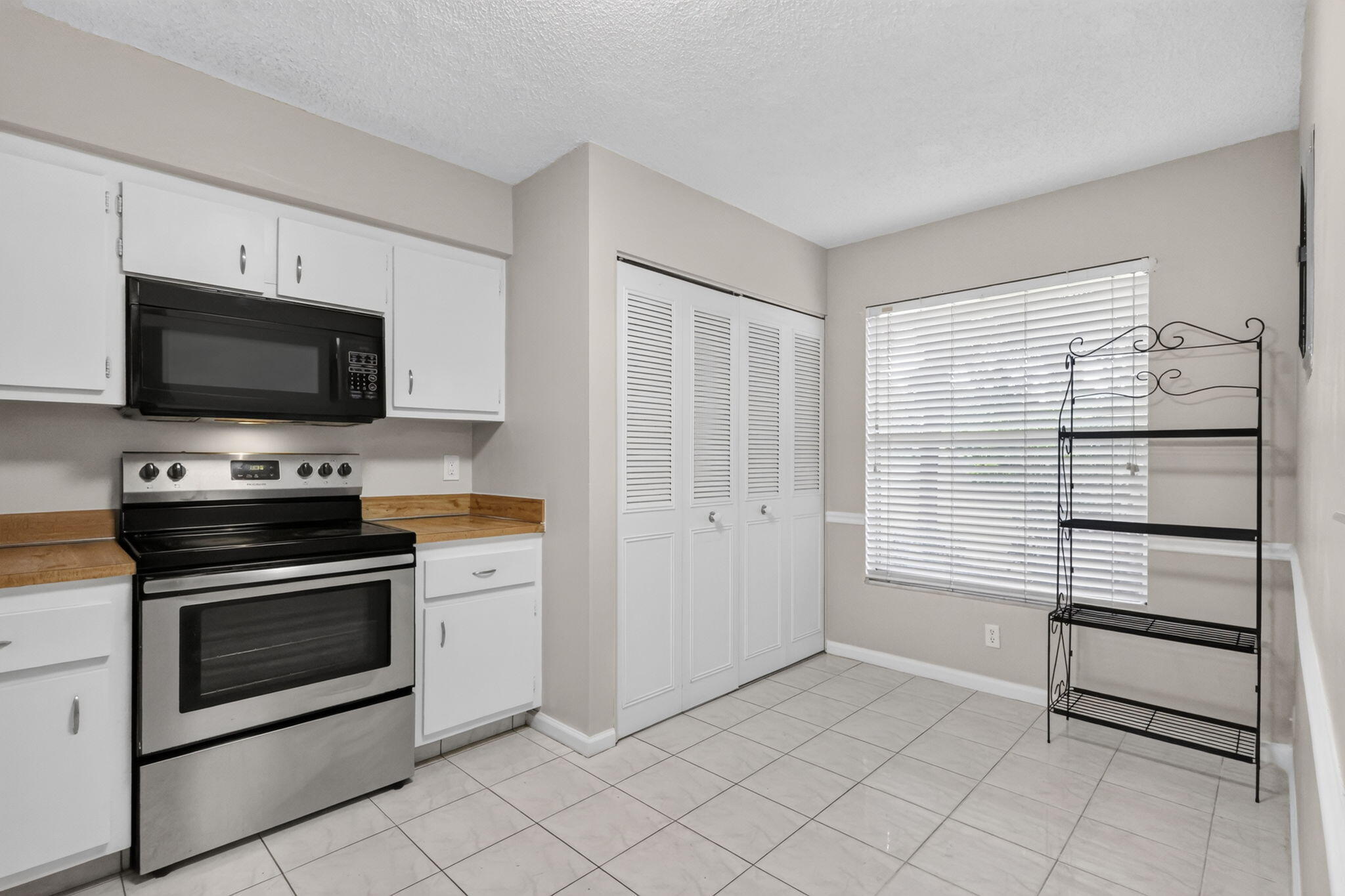 Kitchen area featuring white cabinetry, stainless steel range with overhead microwave, wood-finish countertops, tile flooring, and louvered closet doors