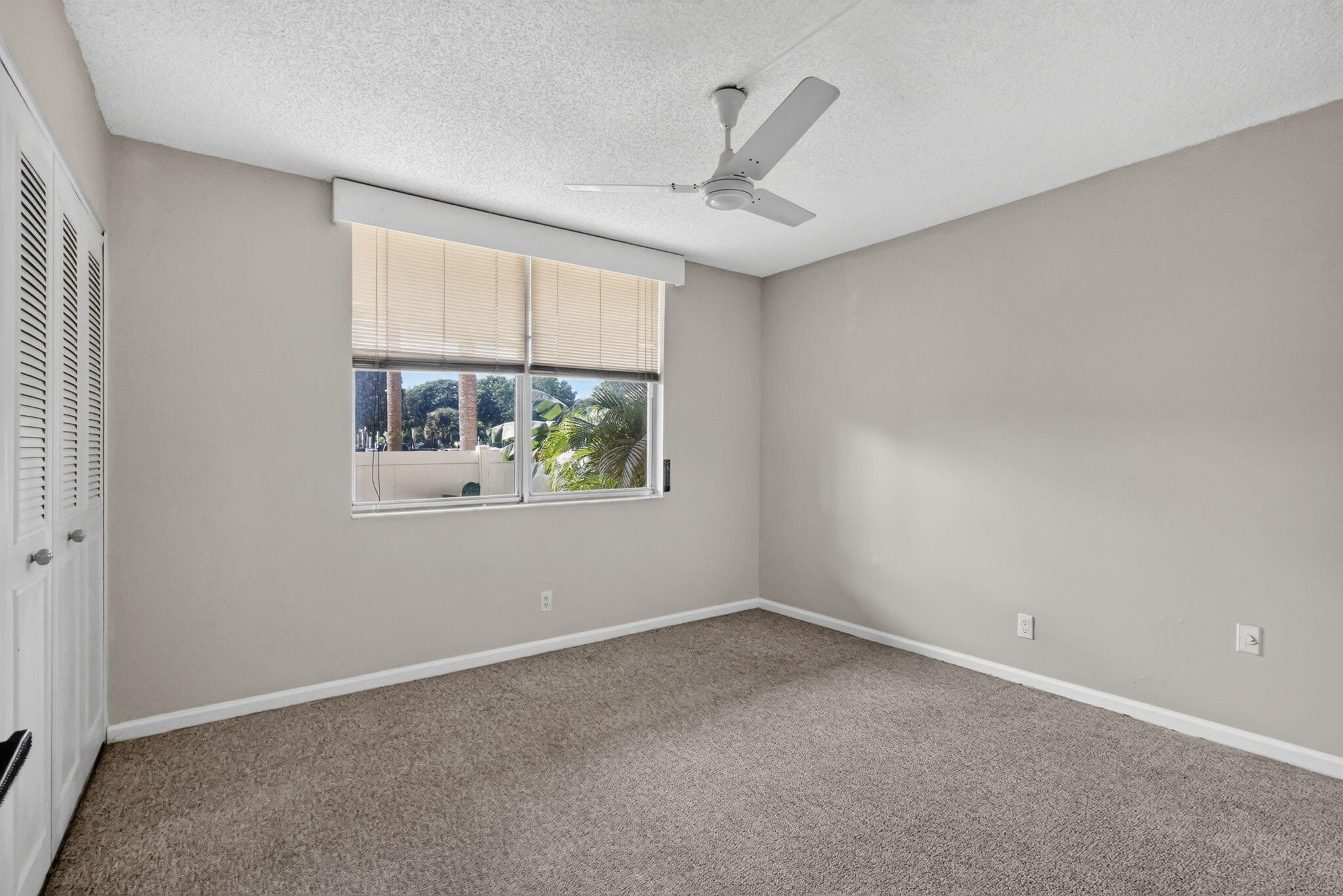 Room featuring neutral wall tones, wall-to-wall carpeting, white bi-fold closet doors, a white ceiling fan, and a window with a valance