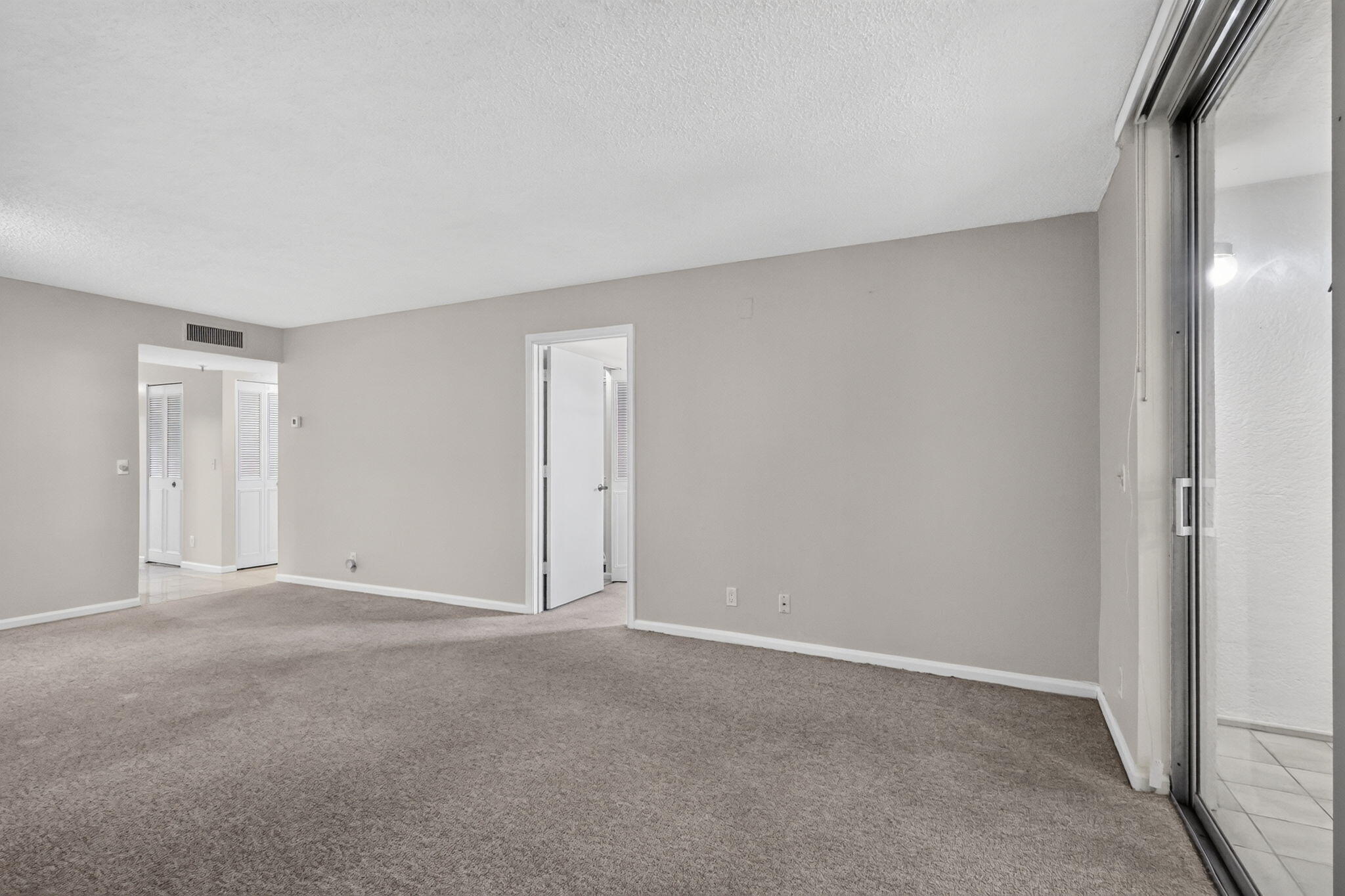 Neutral-toned interior featuring wall-to-wall carpeting, sliding glass doors, and interior doorways with white trim