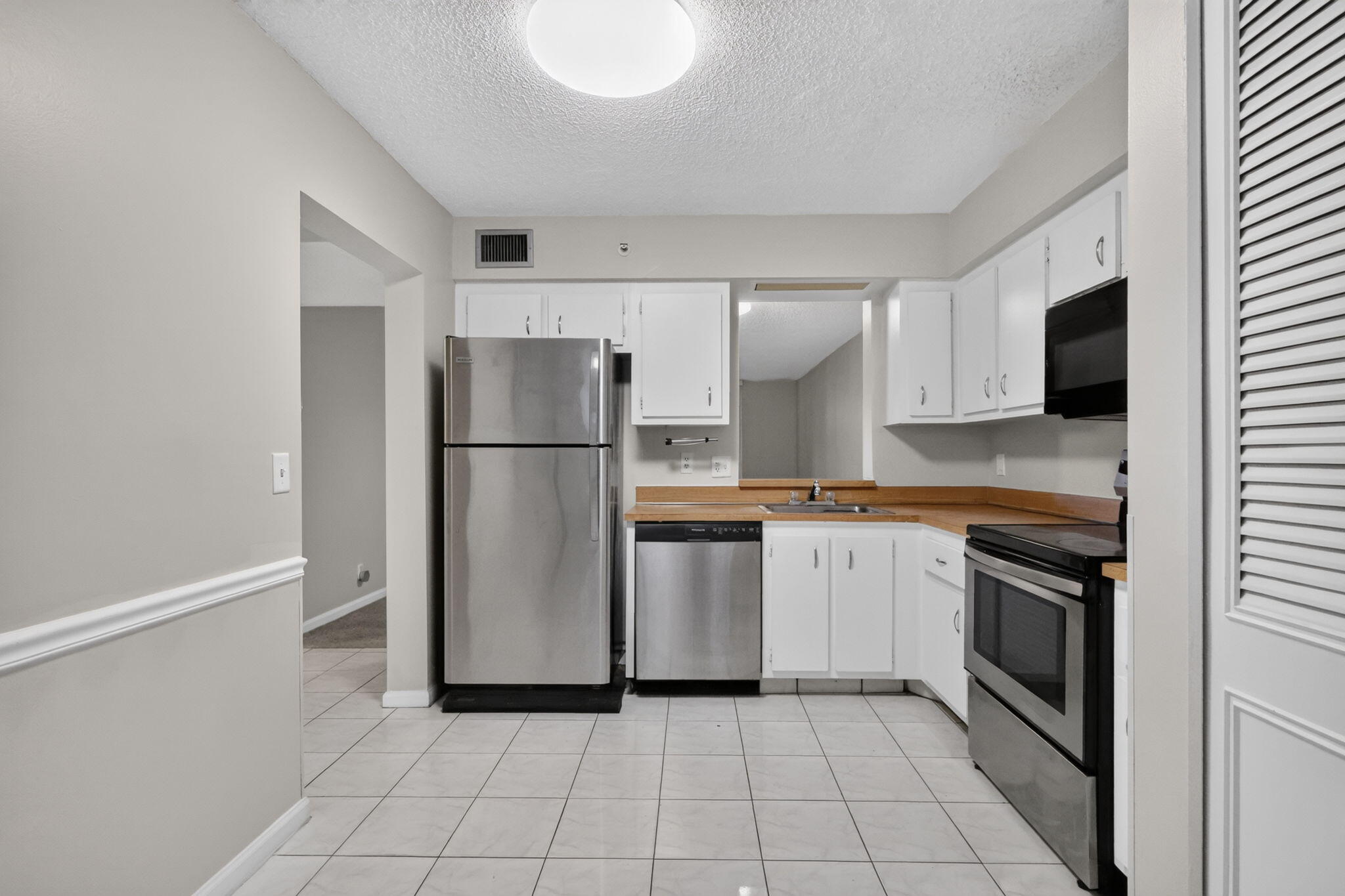 Kitchen featuring white cabinetry, stainless steel appliances, solid-surface countertops, and tile flooring