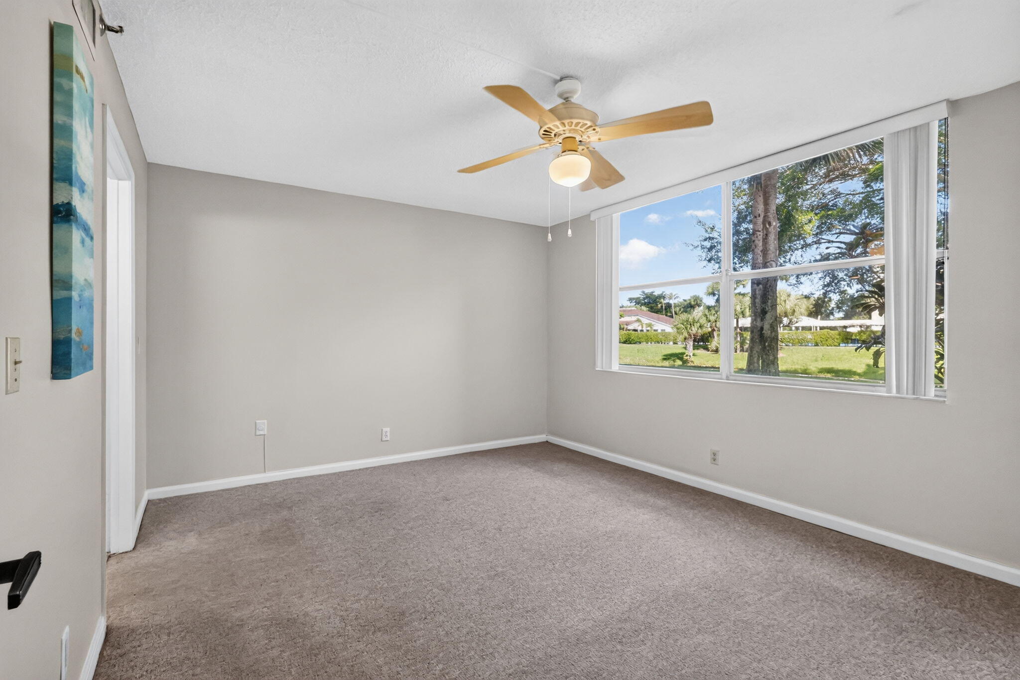 Neutral-toned interior space featuring neutral wall-to-wall carpeting, large multi-pane windows, and a ceiling fan with integrated lighting