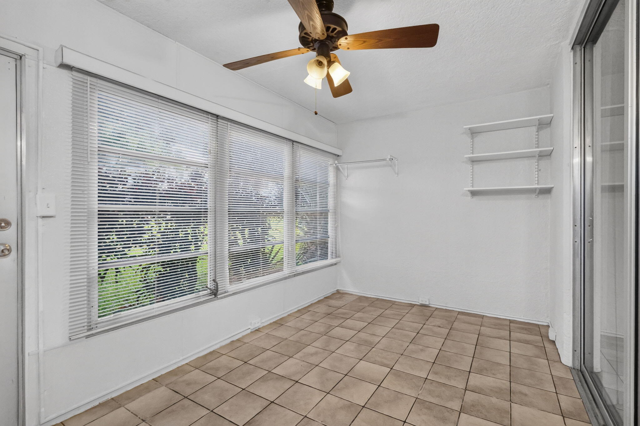 Sunroom featuring large paneled windows, ceramic tile flooring, a ceiling fan with integrated lighting, wall-mounted shelving, and a metal-frame sliding glass door