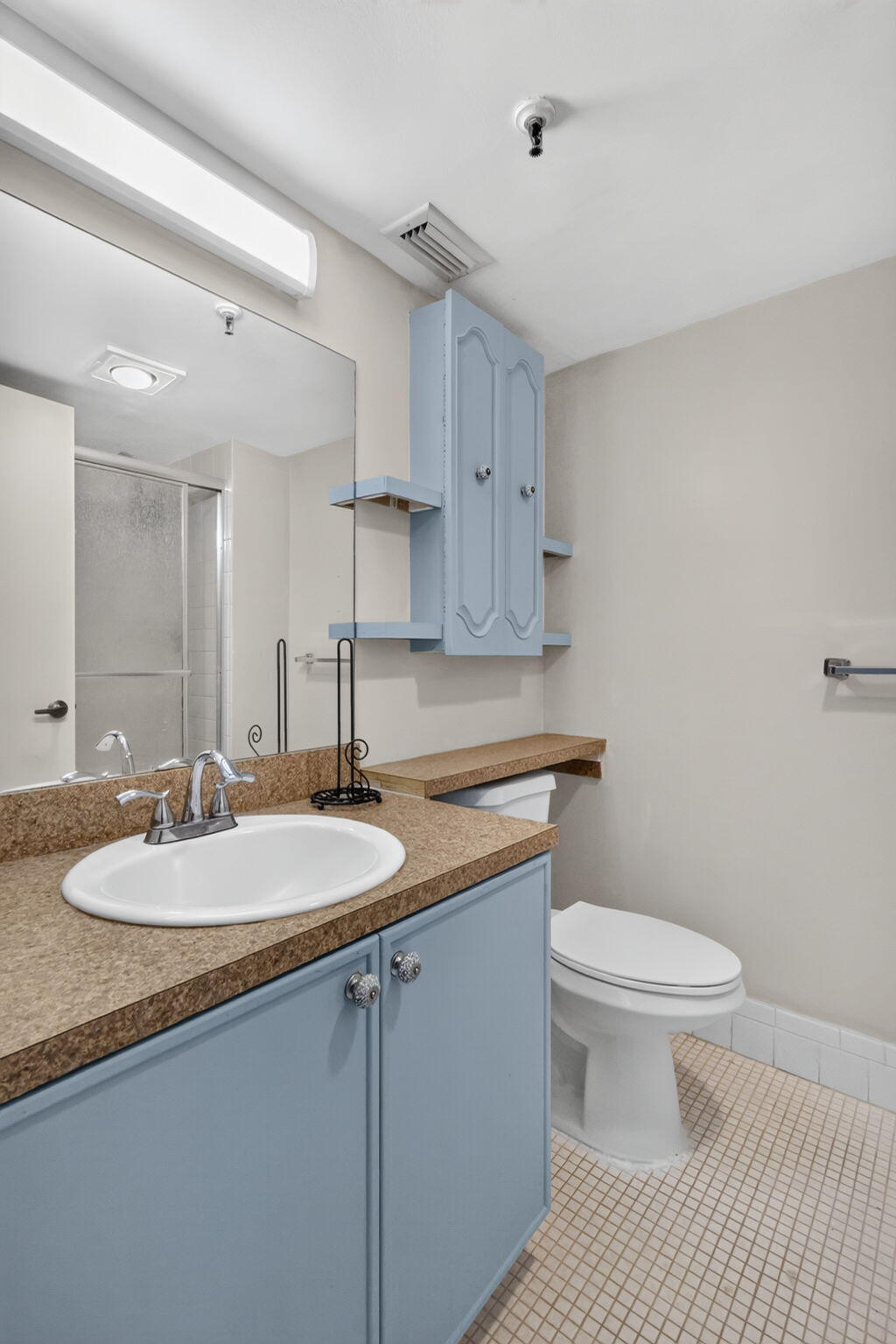 Bathroom featuring a vanity with light blue cabinetry, a neutral solid-surface countertop, an integrated porcelain sink, wall-mounted storage cabinetry, and a large plate-glass mirror
