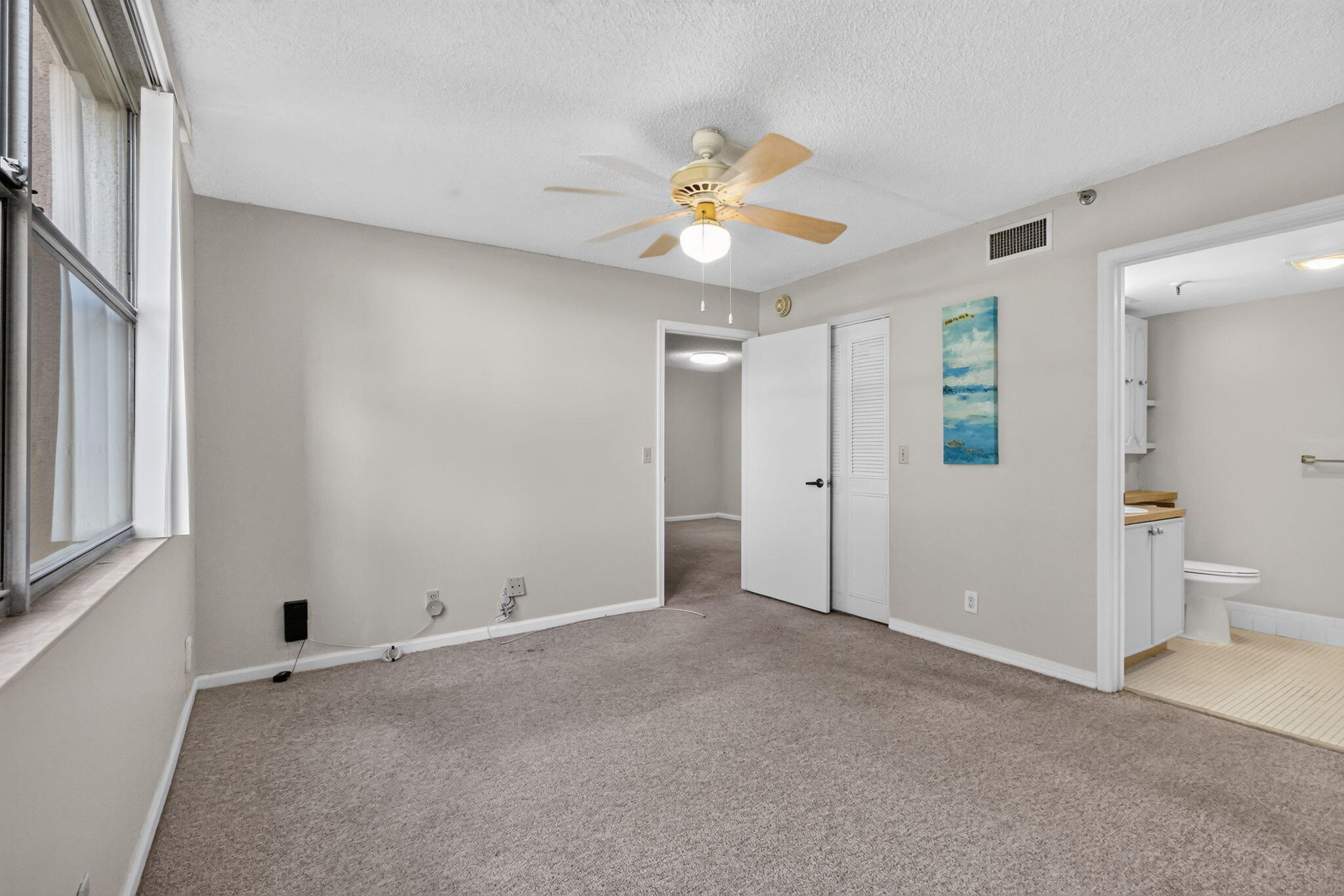 Neutral-toned room featuring wall-to-wall carpeting, a ceiling fan with light fixture, and a white interior door