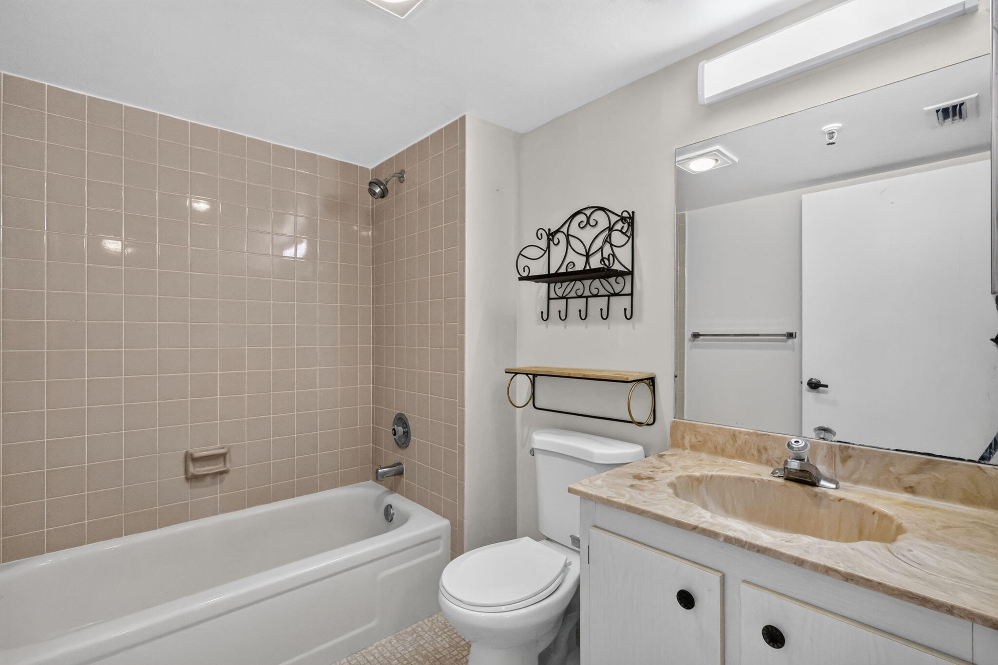 Bathroom featuring a full-sized bathtub with tile surround, stone-composite vanity countertop with an integrated basin, large wall-mounted mirror, and overhead strip lighting