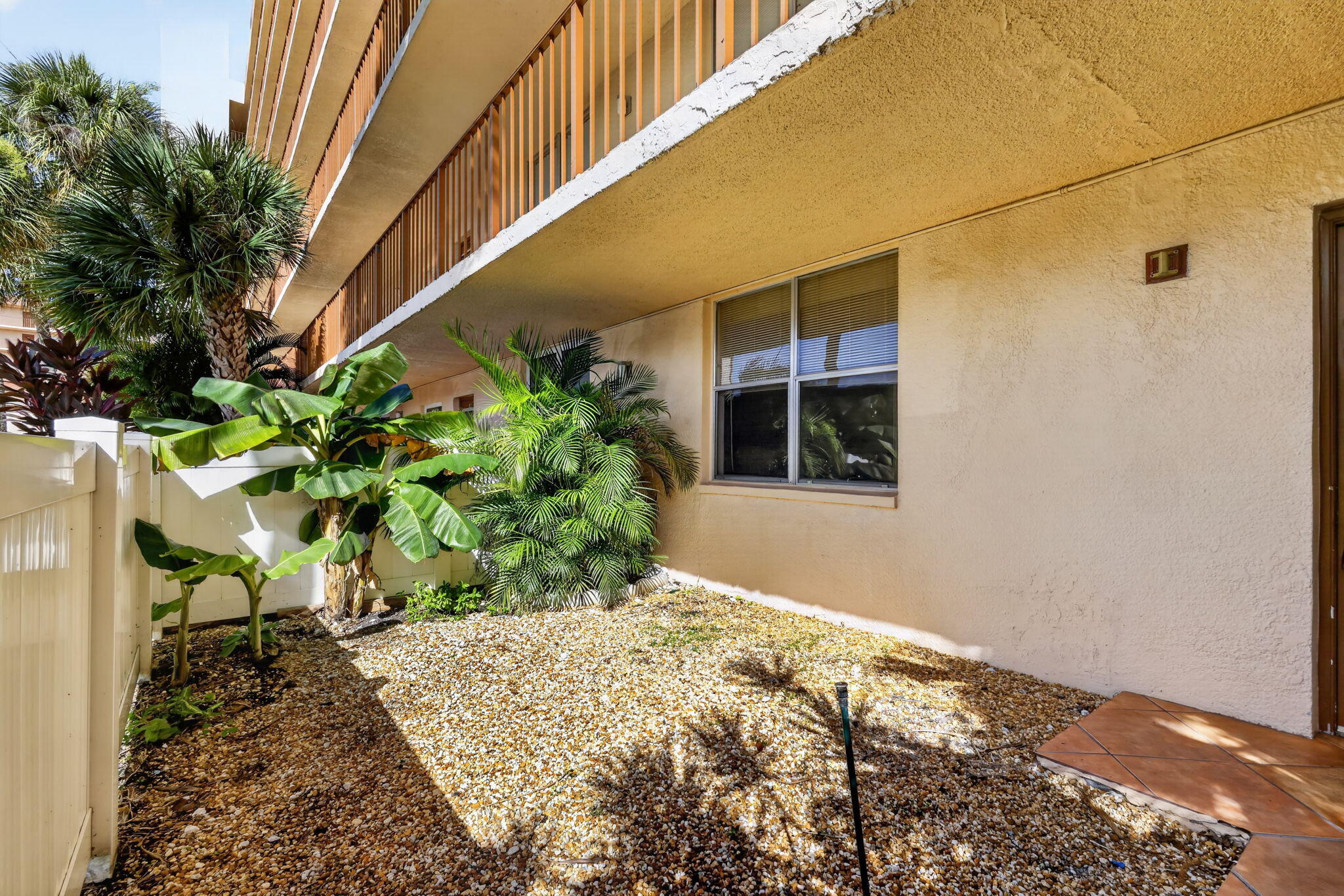 Stucco exterior featuring an elevated balcony with vertical balustrade, paved entrance area, and low-maintenance rock garden