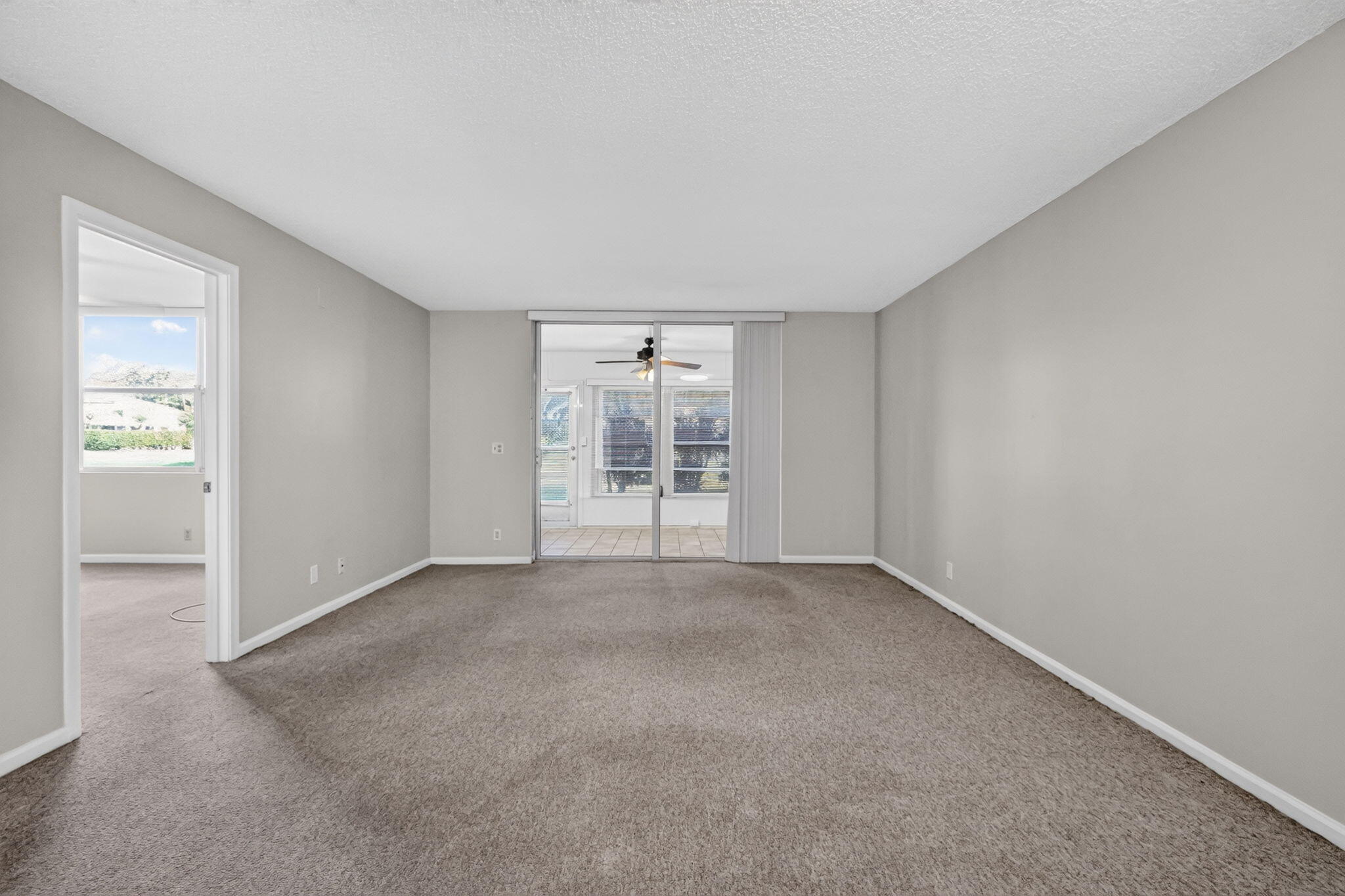 Spacious interior featuring neutral wall tones, carpeted flooring, and a large sliding glass door with access to the enclosed patio