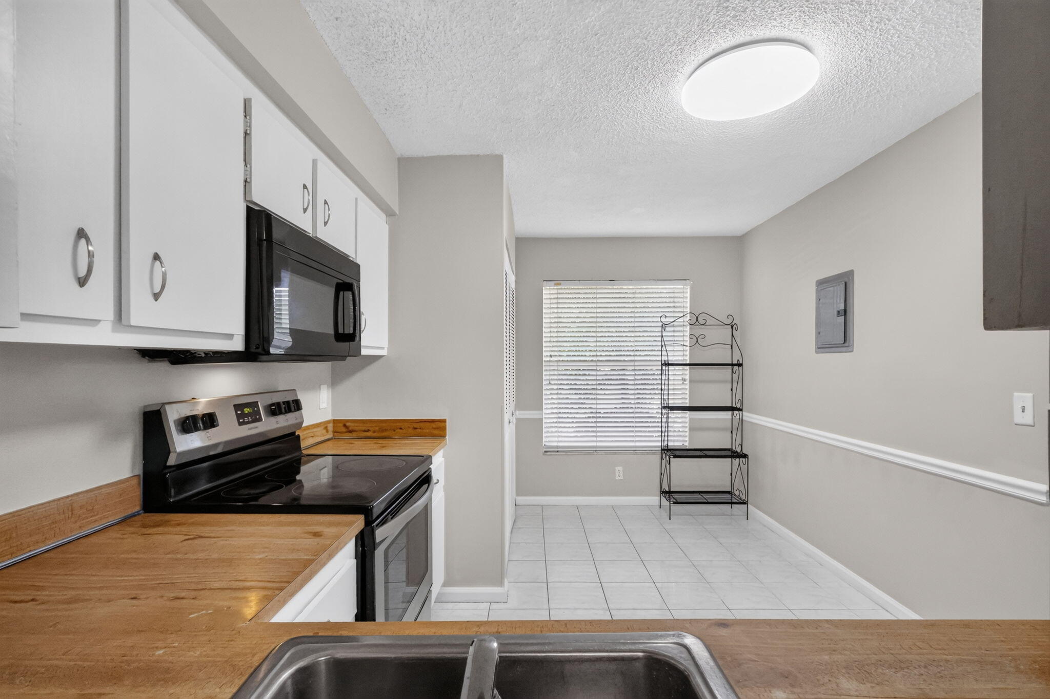 Kitchen featuring white cabinetry, wood-surface countertops, black integrated appliances, tile flooring, and chair rail molding
