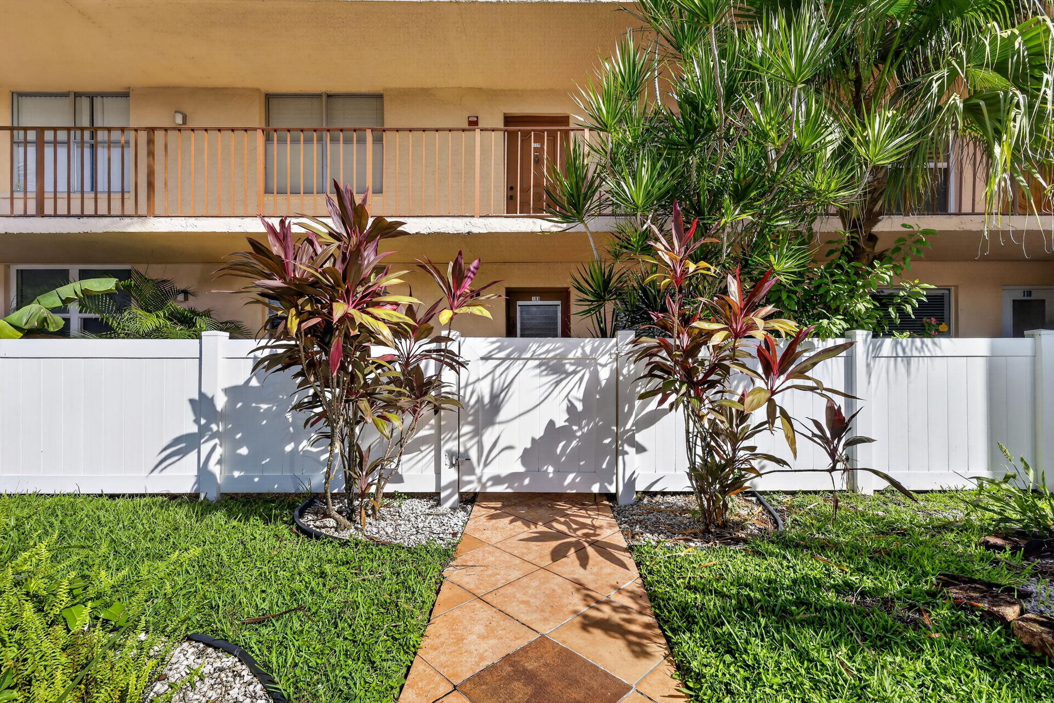 Private patio featuring a white vinyl privacy fence, terracotta-toned paver walkway, and integrated landscaping