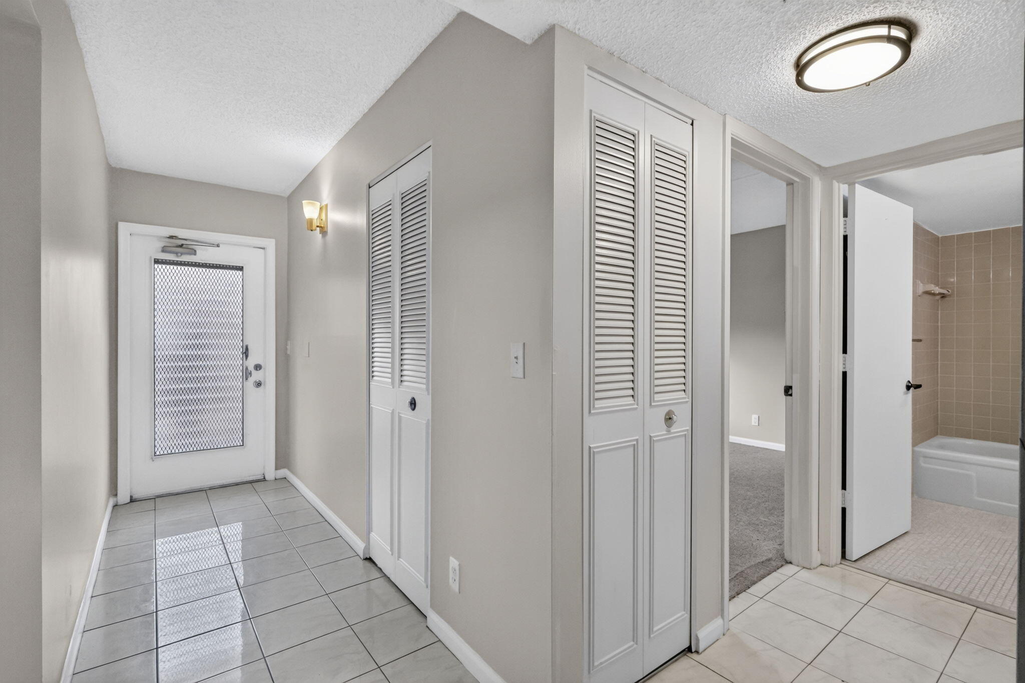 Entrance foyer featuring large-format ceramic tile flooring, double-panel louvered closet doors, and flush-mount ceiling lighting