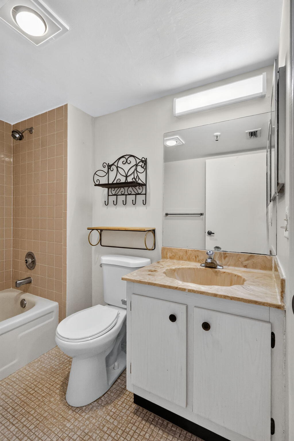 Bathroom featuring a vanity with stone-surfaced countertop, integrated sink, tiled tub surround, full-width mirror, and overhead lighting