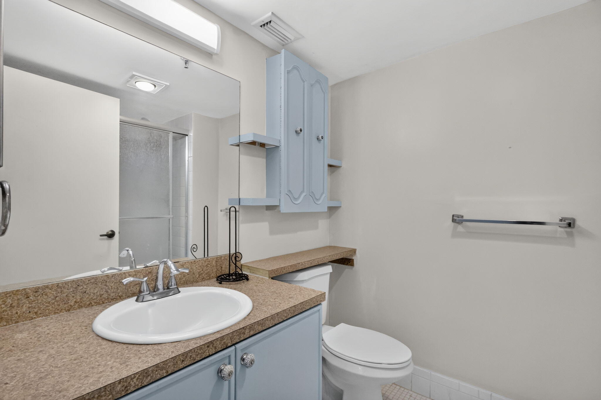 Bathroom featuring a vanity with a solid-surface countertop, an integrated oval sink, wall-mounted cabinetry with side shelving, a full-width mirror, and a glass-enclosed shower