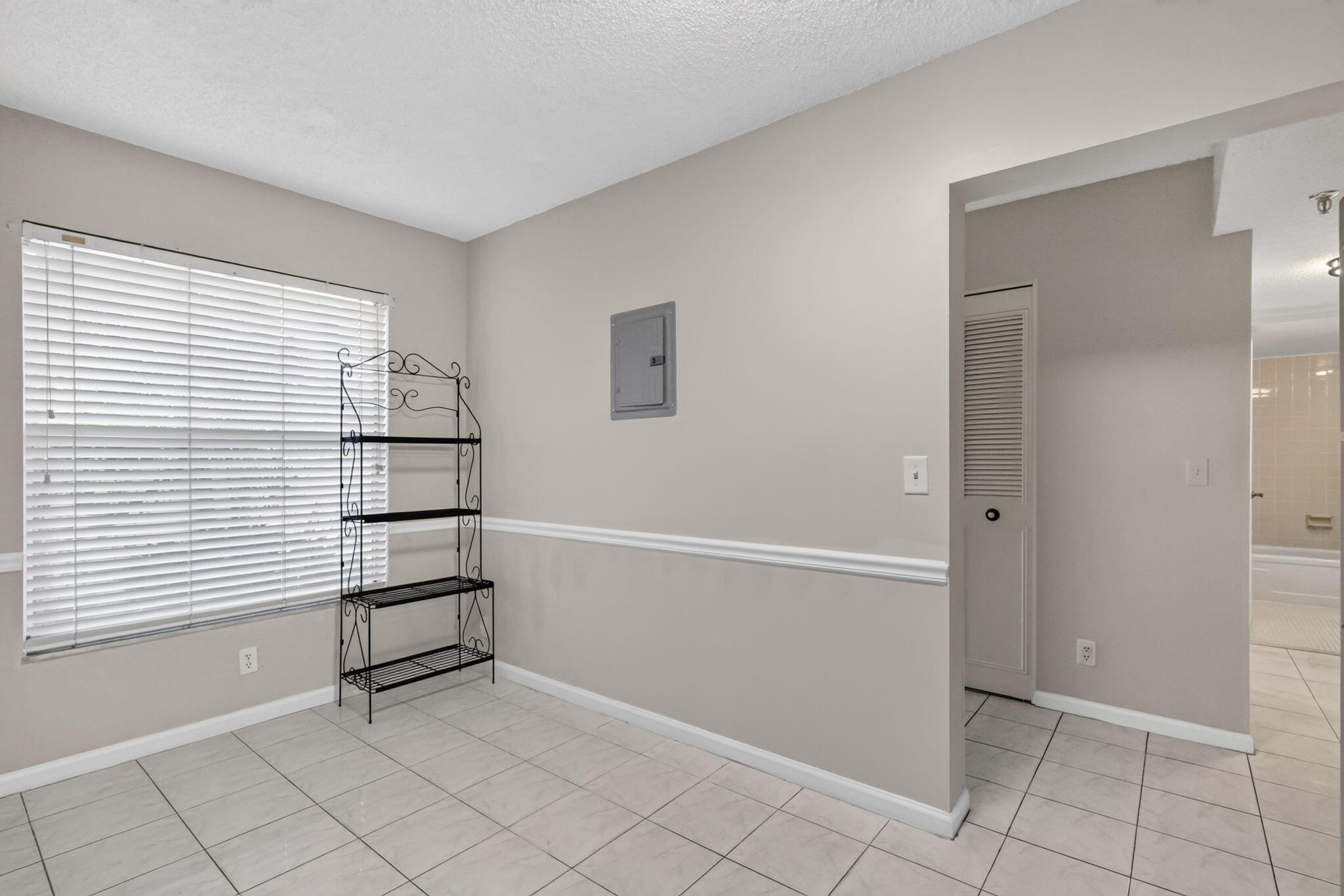 Neutral-toned interior featuring ceramic tile flooring, horizontal window blinds, chair rail molding, and a louvered closet door