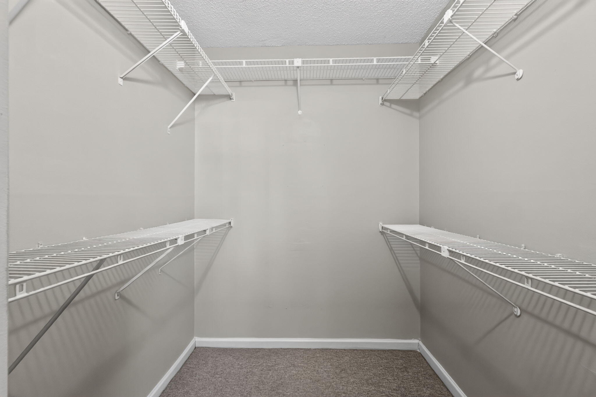 Walk-in storage space featuring neutral wall paint, high-density carpeting, and tiered white wire shelving
