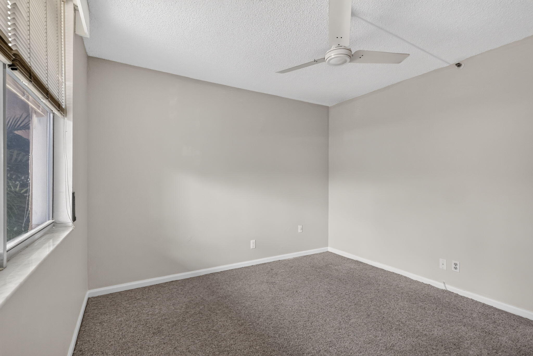 Neutral-toned interior space featuring wall-to-wall carpeting, a multi-blade ceiling fan, and horizontal window blinds