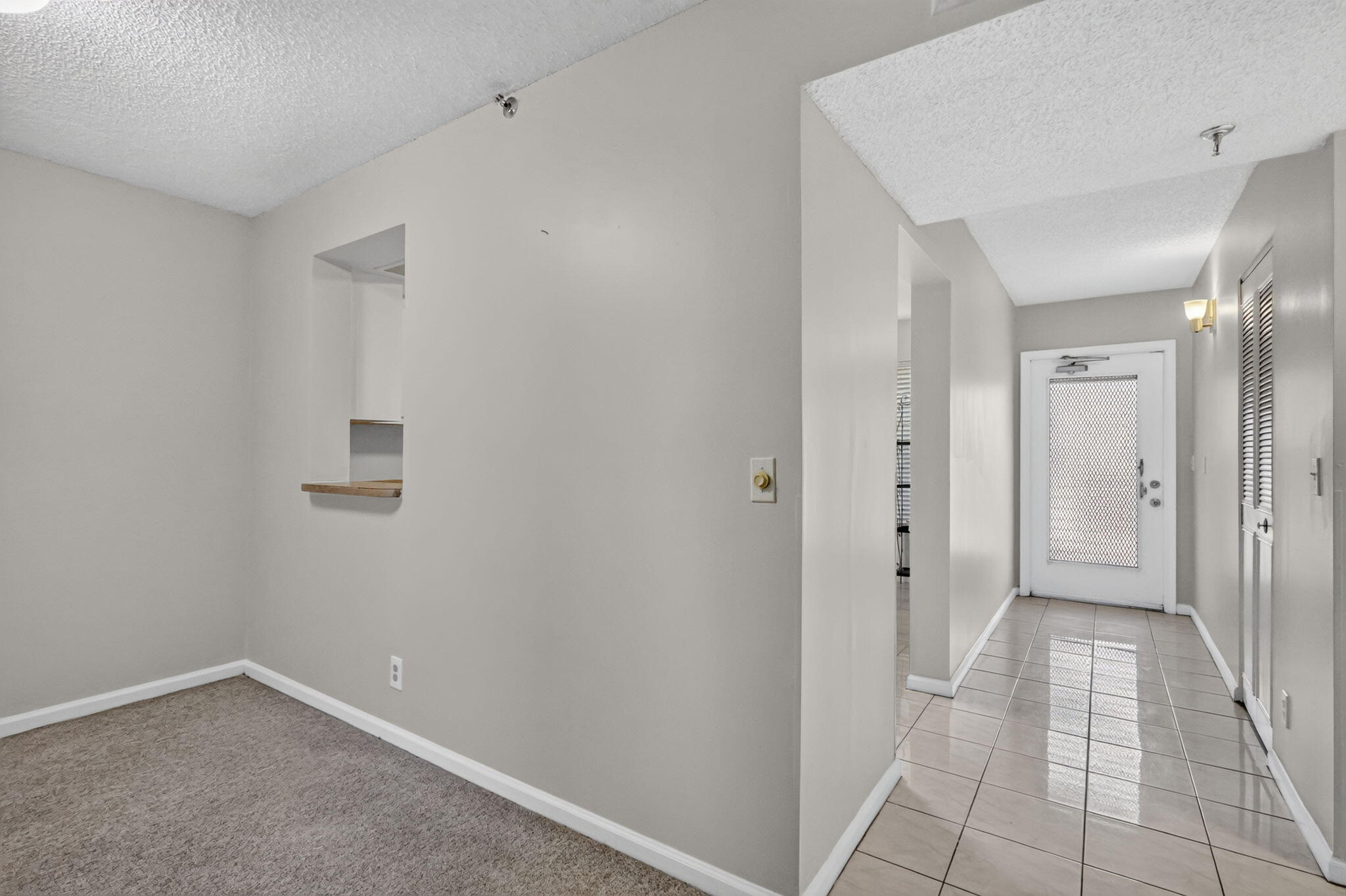 Interior hallway featuring ceramic tile flooring, a pass-through window with a wood-finish ledge, neutral wall paint, and a door with an inset textured glass panel