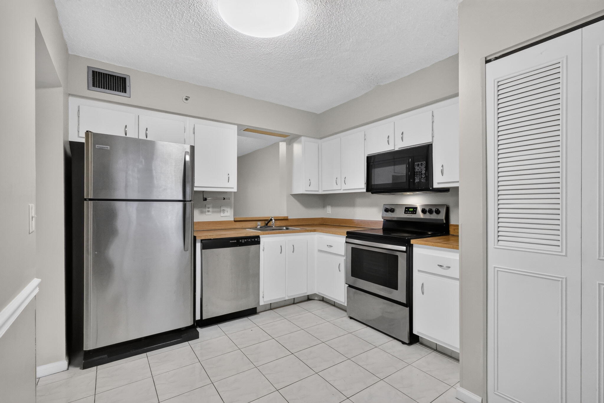 Kitchen featuring white cabinetry, stainless steel appliances, butcher block countertops, and tiled flooring
