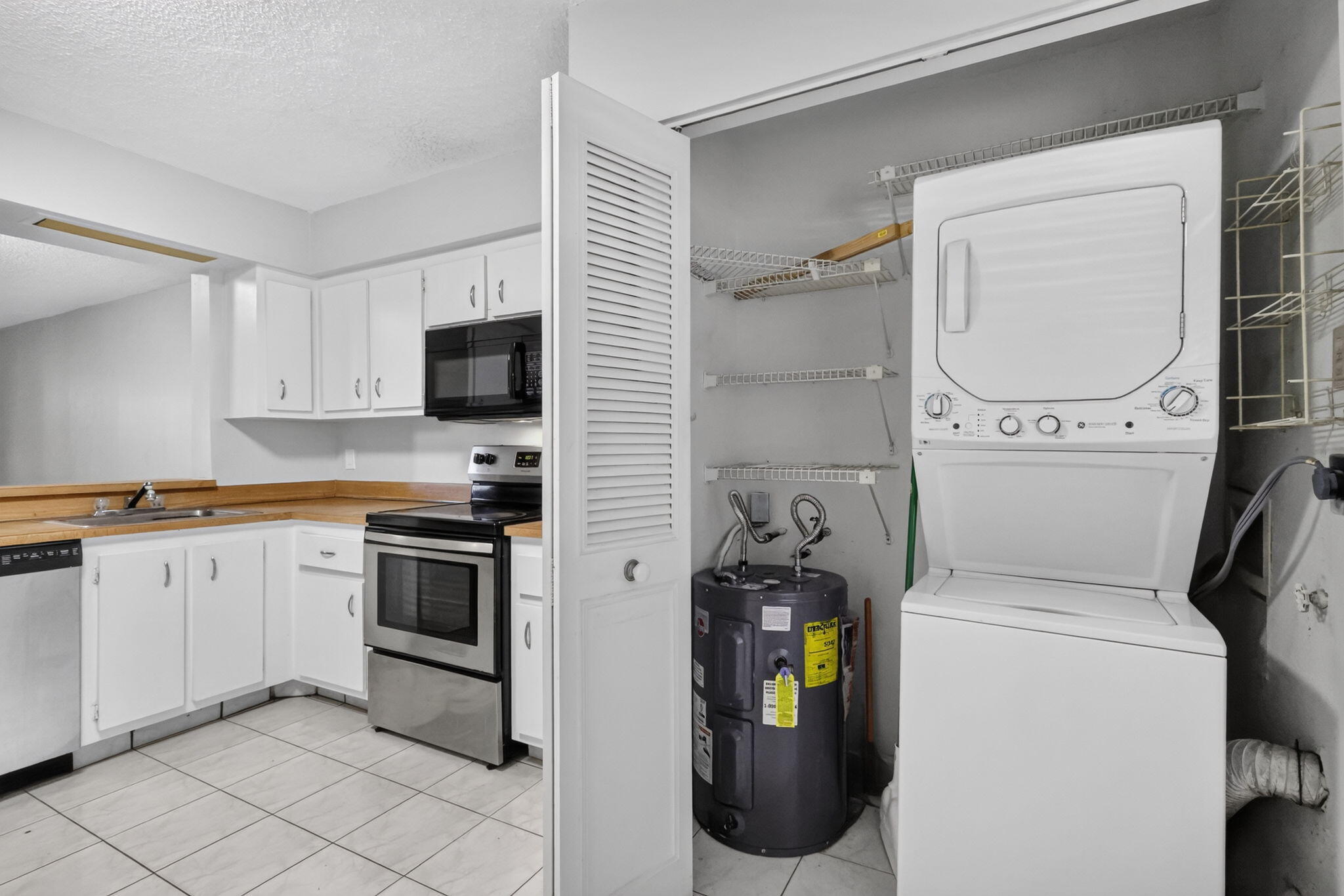 Kitchen featuring white cabinetry, stainless steel appliances, tile flooring, and an integrated laundry closet with a stacked washer and dryer unit