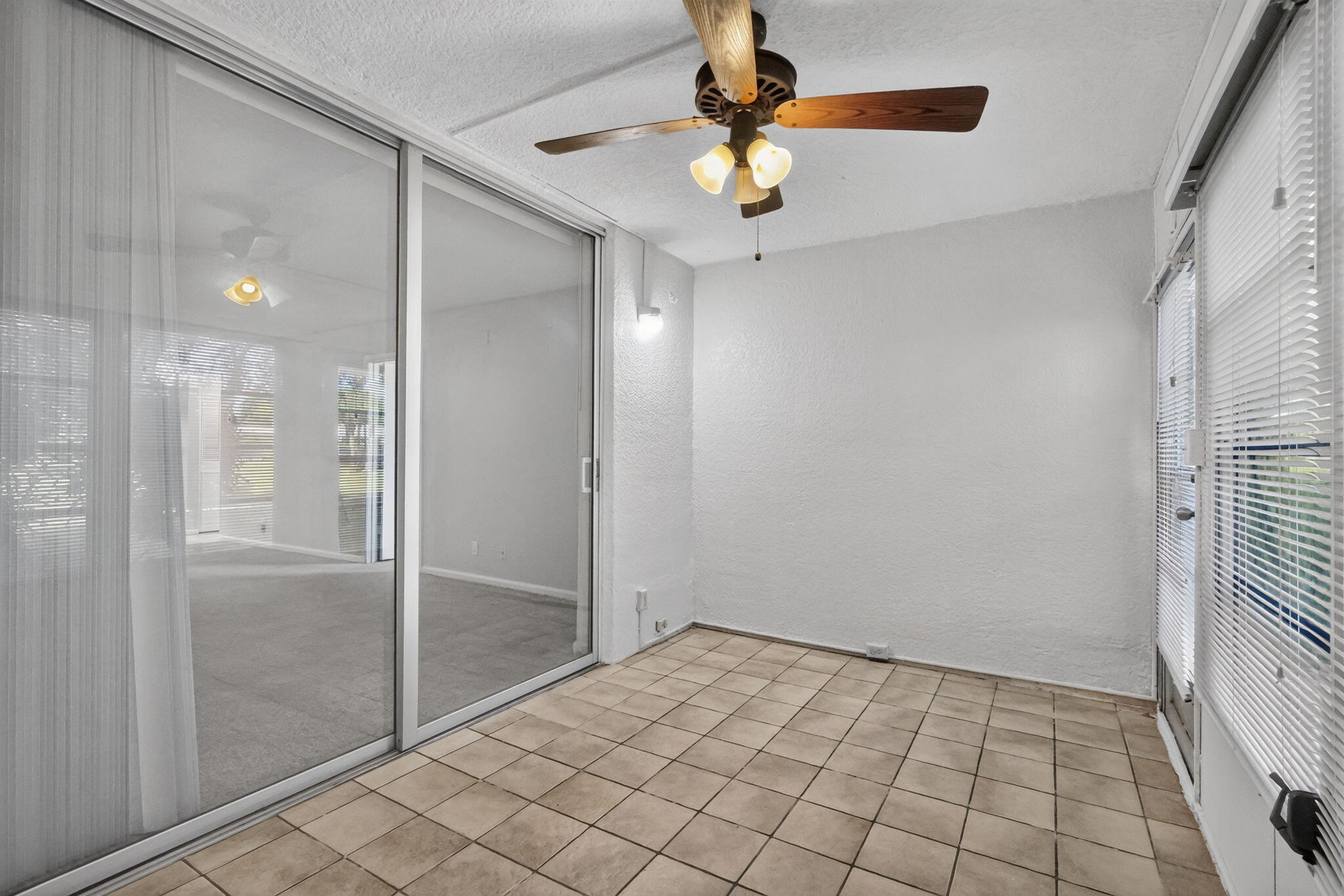 Enclosed porch featuring ceramic tile flooring, textured wall finishes, a ceiling fan with integrated lighting, and large sliding glass doors