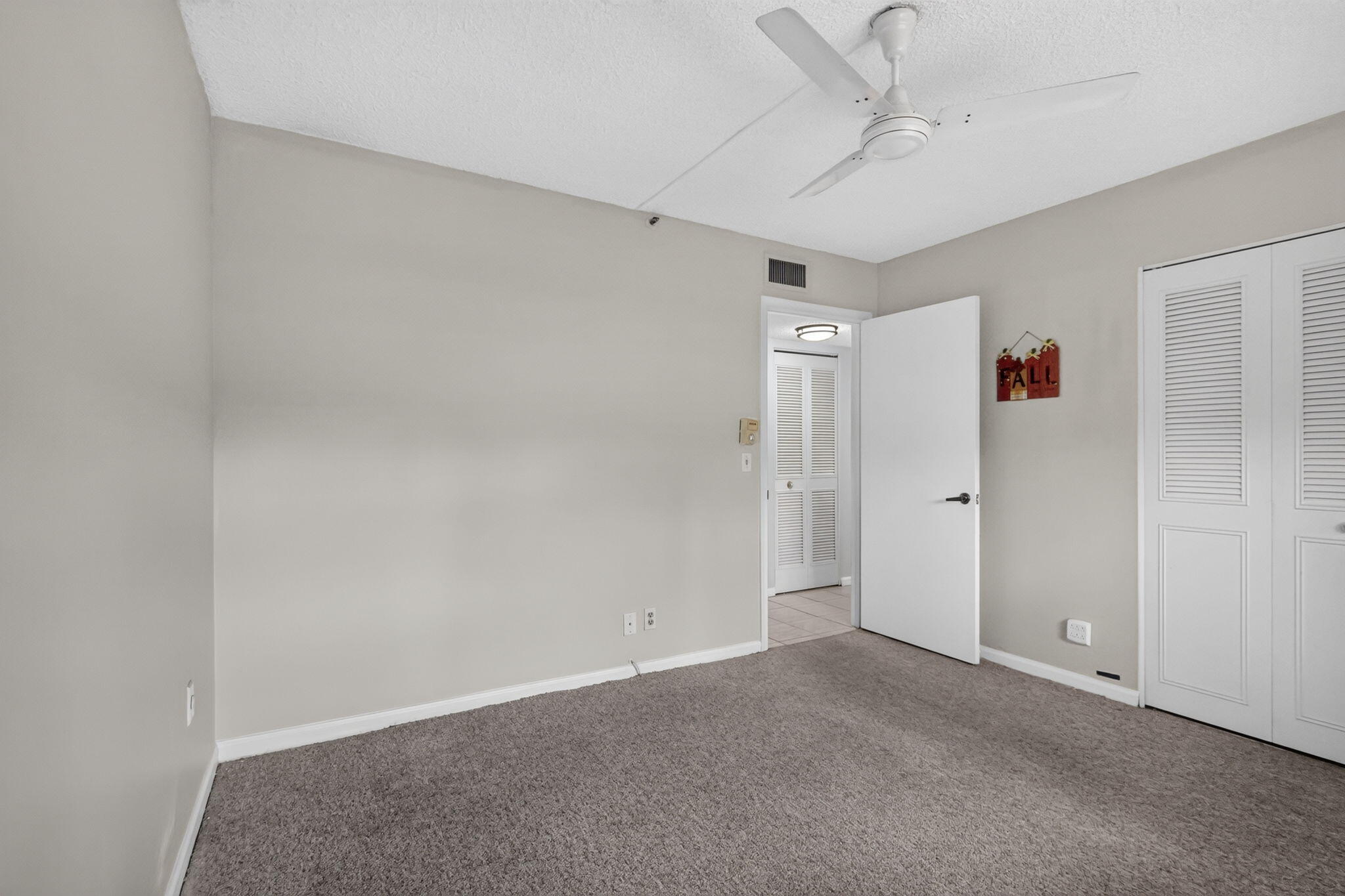 Neutral-toned interior featuring wall-to-wall carpeting, a white ceiling fan, and double-door louvered closet