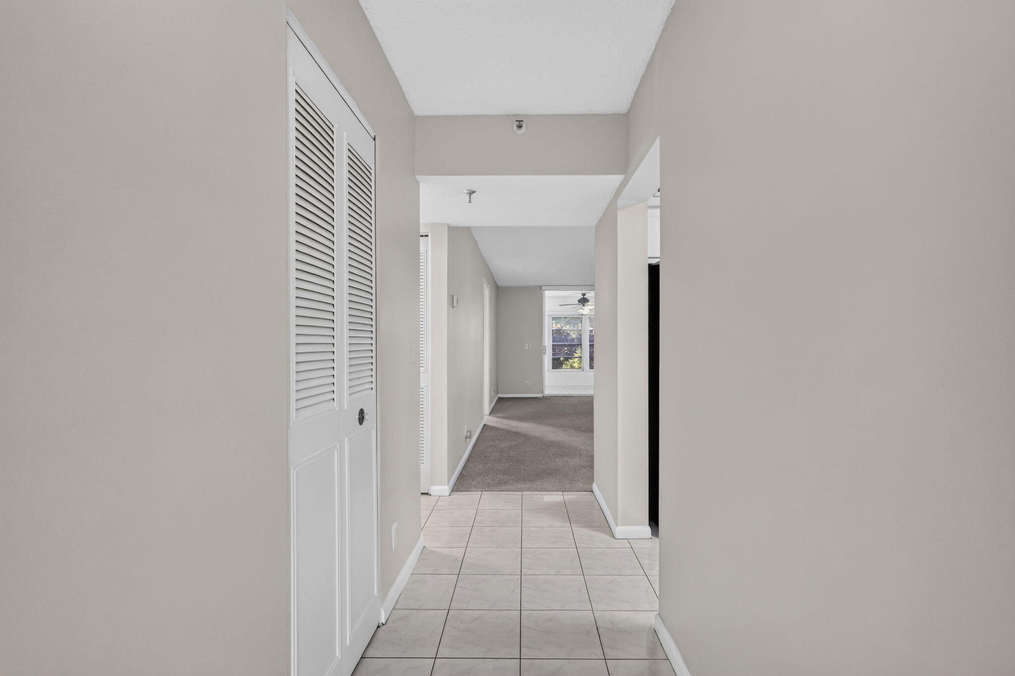 Hallway featuring light-toned ceramic tile flooring, neutral wall paint, and floor-to-ceiling closet with white louvered double doors