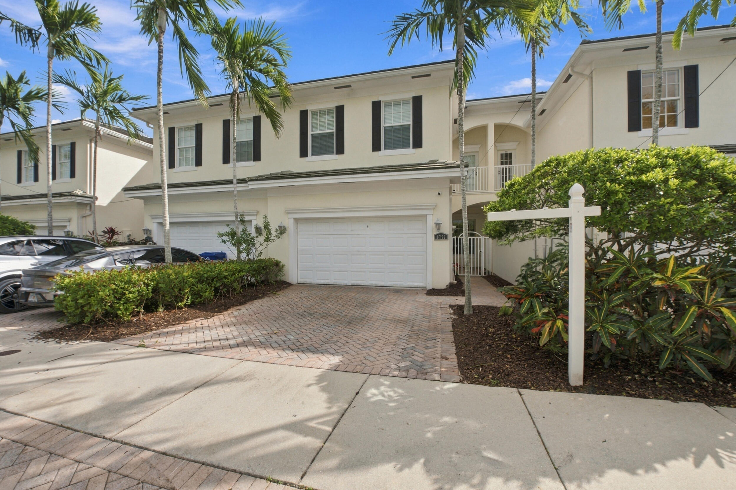 Two-story exterior featuring light-toned stucco, dark shutters, a paved driveway, and an attached garage