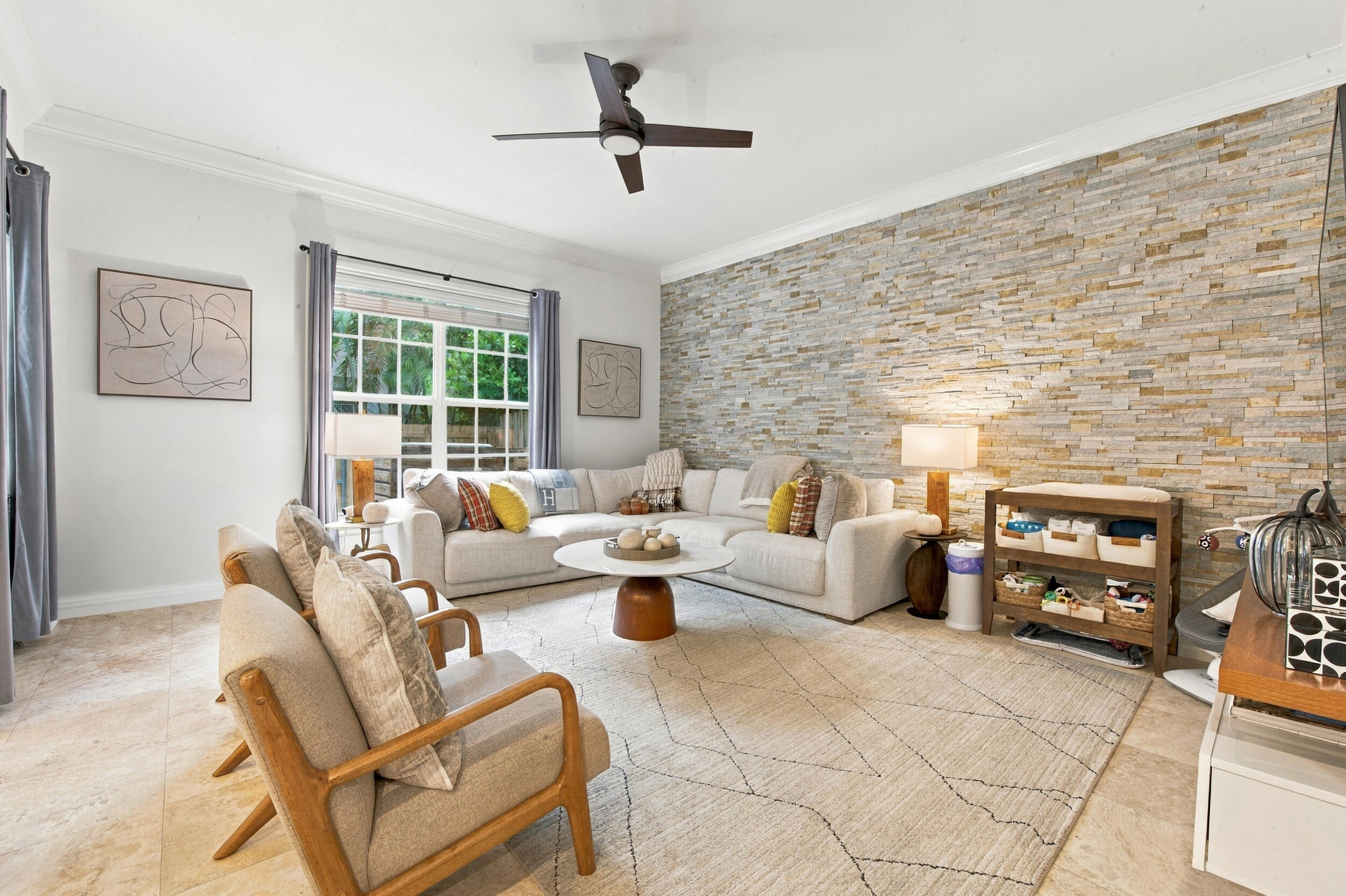 Living area featuring a stacked stone accent wall, tile flooring, crown molding, and a ceiling fan