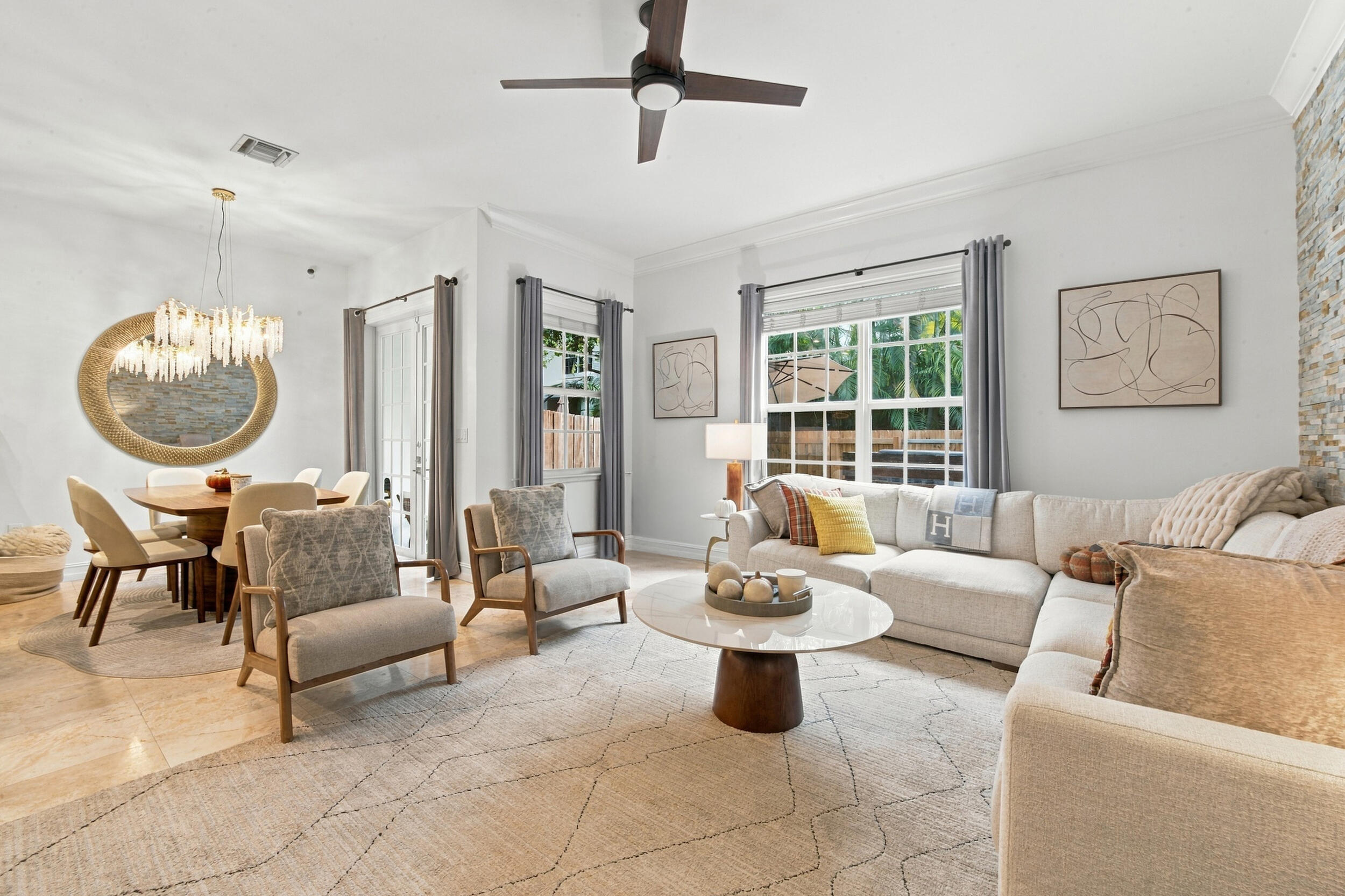 Open living area featuring large-format tile flooring, a stone-accented wall, crown molding, multi-light chandelier, and ceiling fan