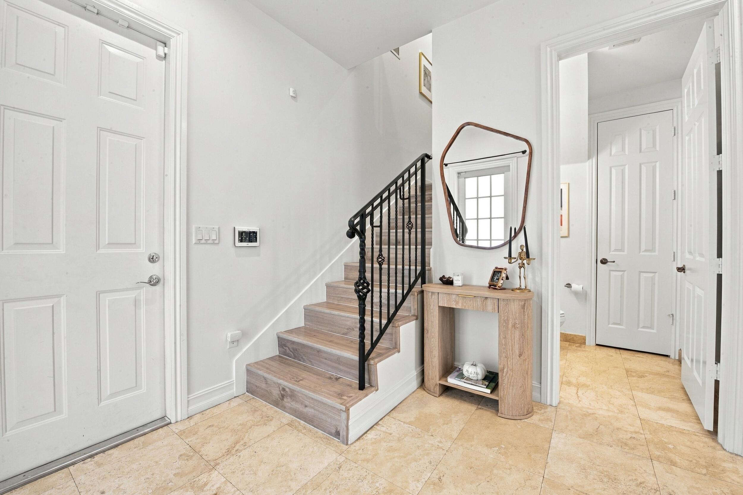 Entryway featuring large-format tile flooring, staircase with wood-finish treads, and black iron balustrade
