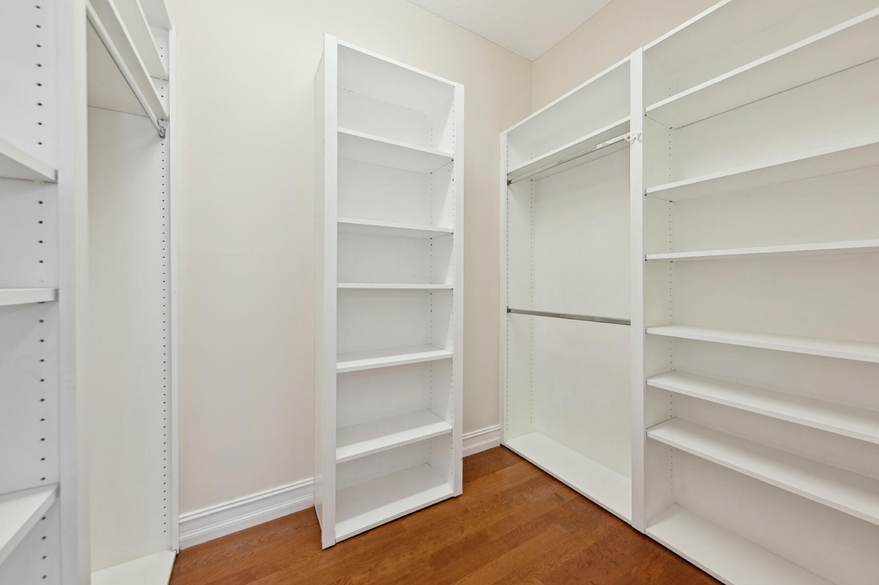 Custom walk-in closet featuring floor-to-ceiling white shelving units, integrated hanging rods, and wood-finish flooring