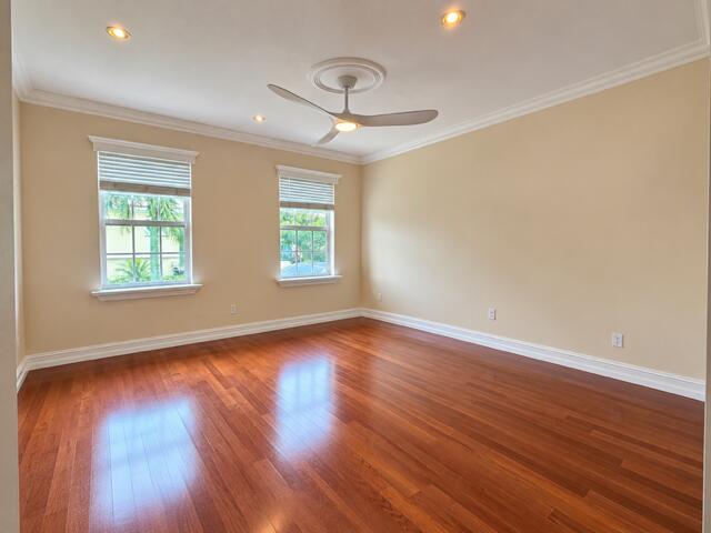 Room featuring wood-finish flooring, recessed lighting, crown molding, double windows with window treatments, and a central ceiling fan with a medallion