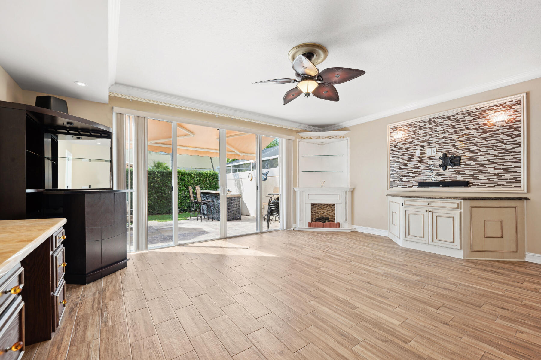 Living space featuring wood-finish flooring, a corner fireplace with built-in shelving, a stone-tiled media wall, multi-panel glass sliding doors, and a ceiling fan with integrated lighting