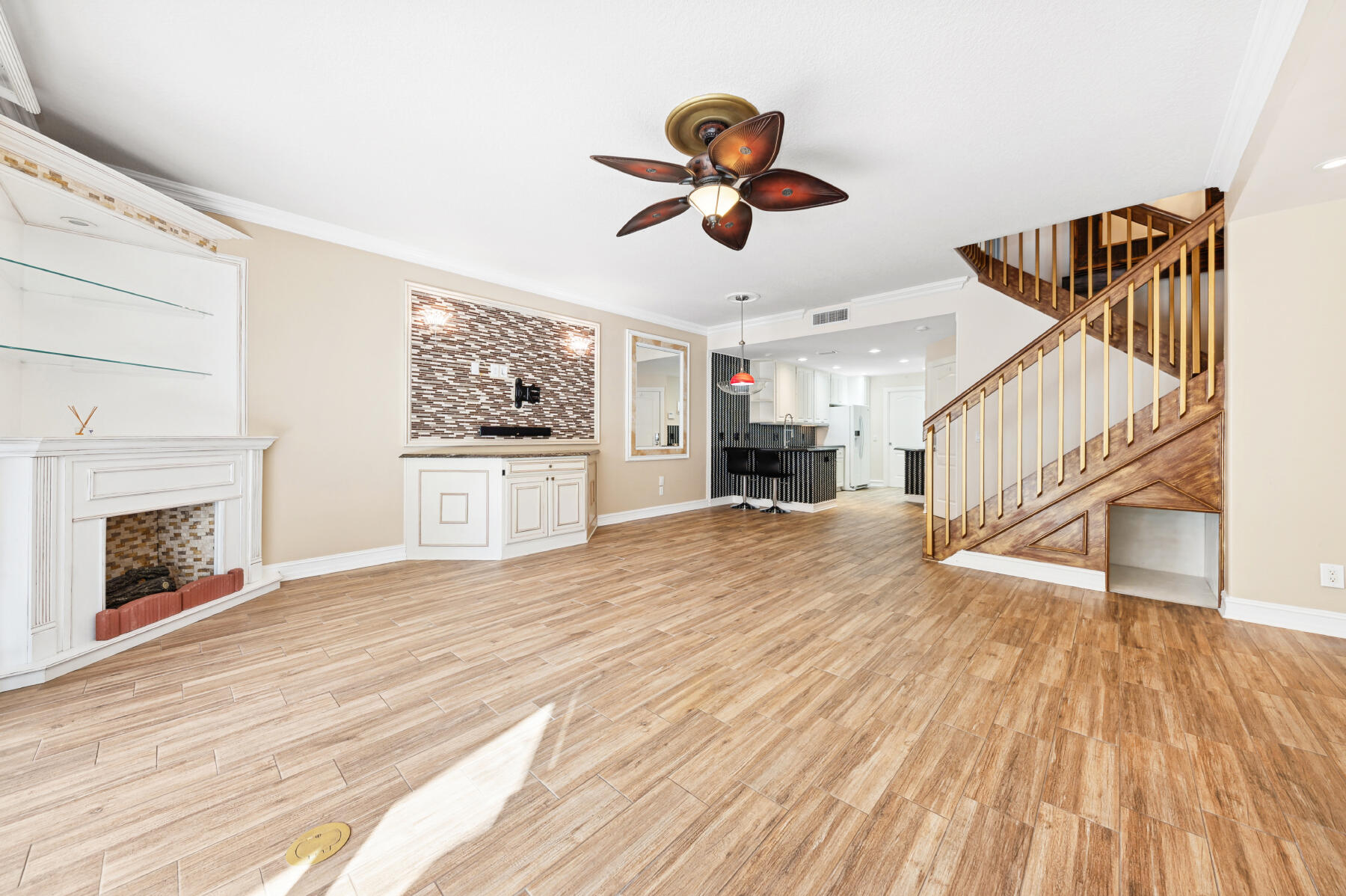 Wood-finish flooring, fireplace with stone-tile surround, custom built-in cabinetry, decorative ceiling fan, and wooden staircase with metal balusters