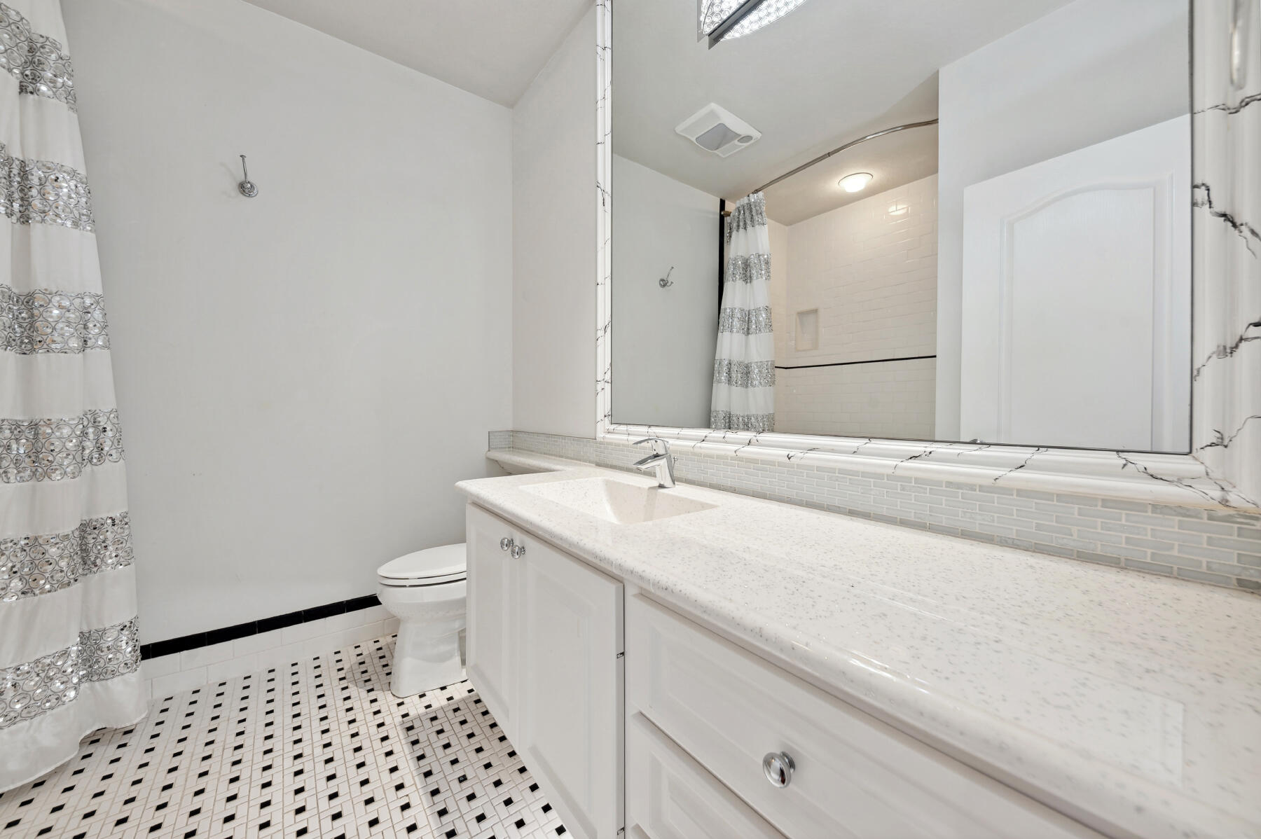 Bathroom featuring a vanity with a light-toned solid surface countertop, an integrated rectangular sink, a large framed mirror, and mosaic-style floor tiling
