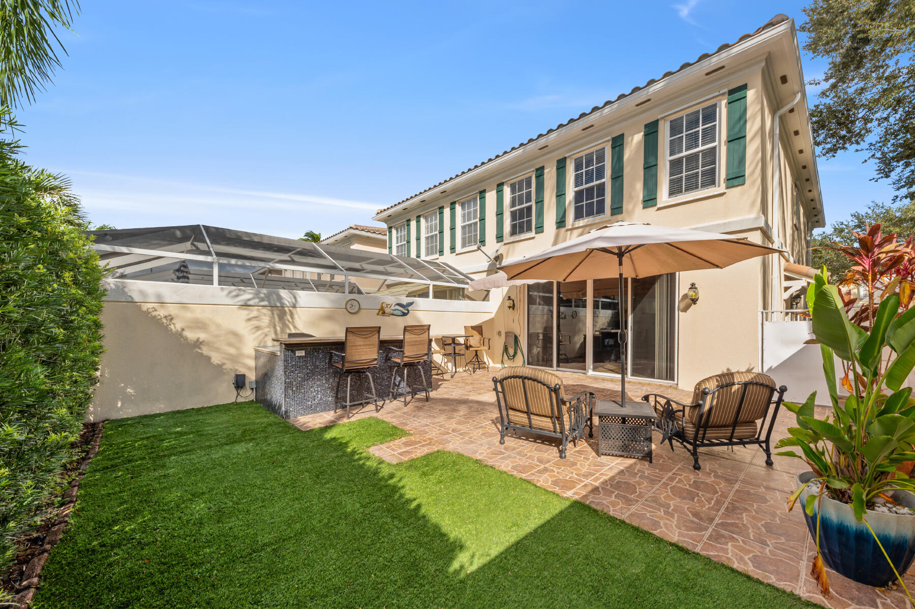 Exterior patio featuring a stone-tile floor, outdoor bar with a stone-finish counter, synthetic turf area, and screened-in enclosure