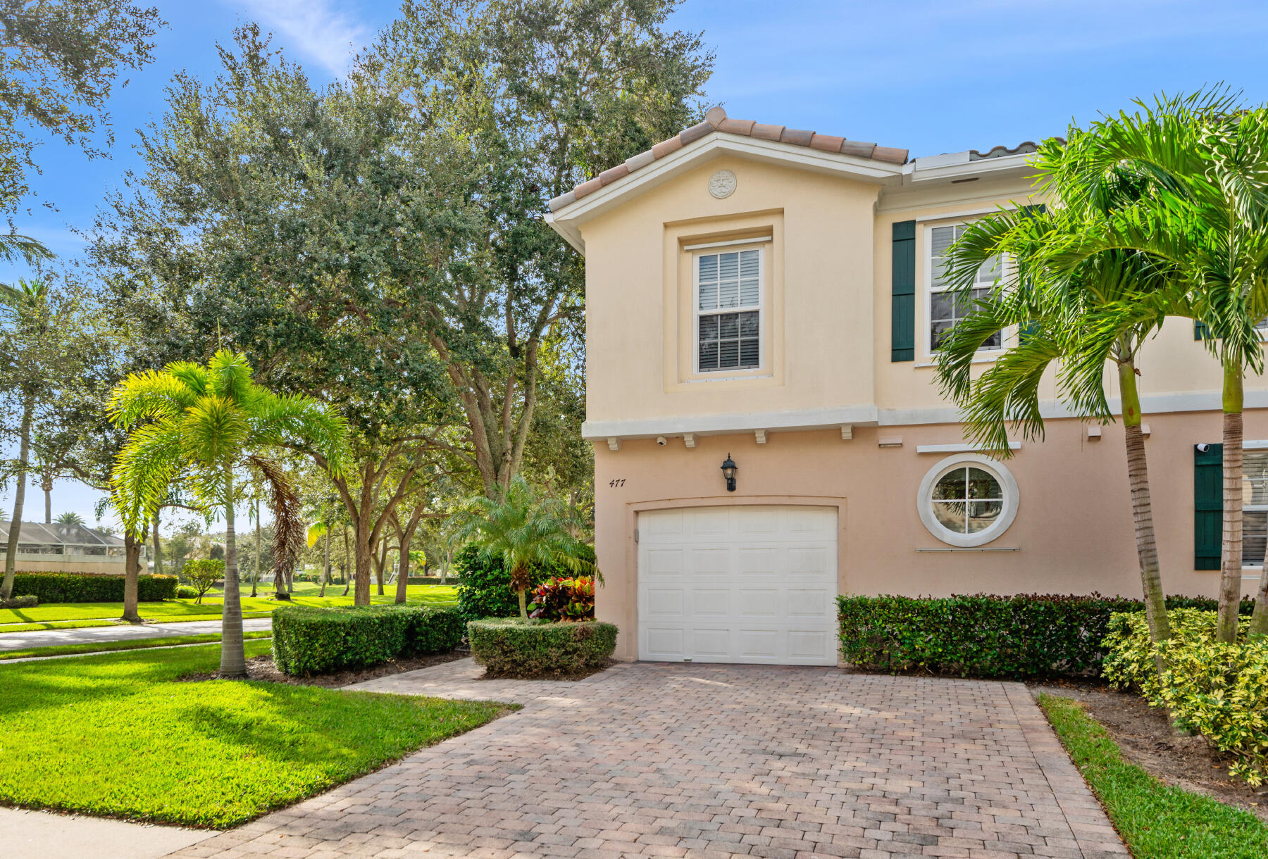 Two-story residence featuring a paved stone driveway, single-car garage, stucco exterior, accent shutters, and circular window detailing