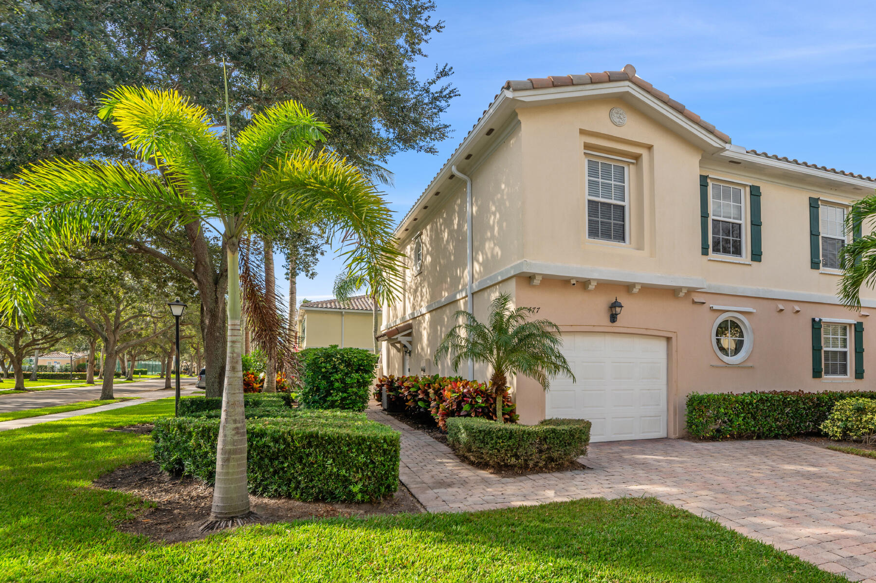 Two-story stucco exterior featuring a paved stone driveway, decorative shutter accents, a circular window, and manicured landscaping