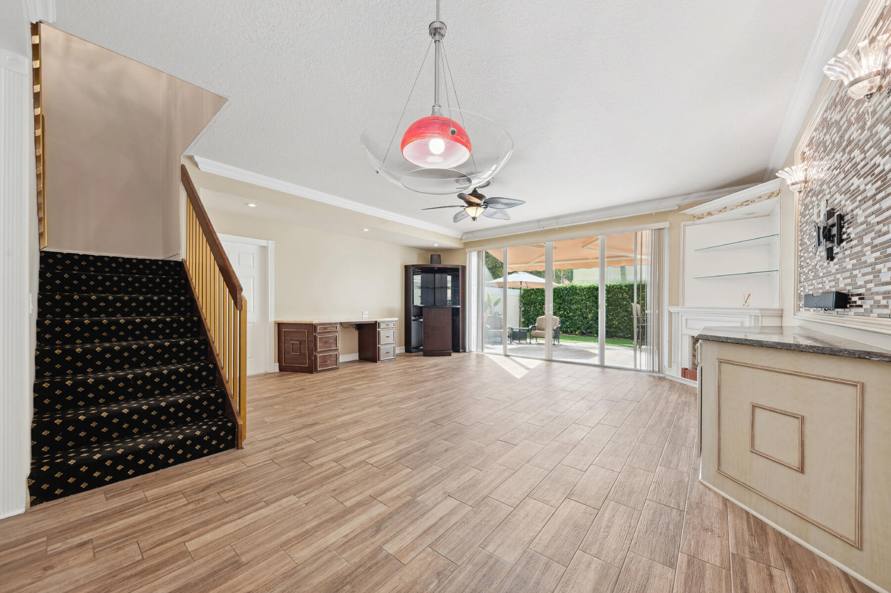 Open-concept interior featuring wood-finish flooring, a built-in stone-top wet bar, floor-to-ceiling glass sliding doors, and a decorative tile accent wall