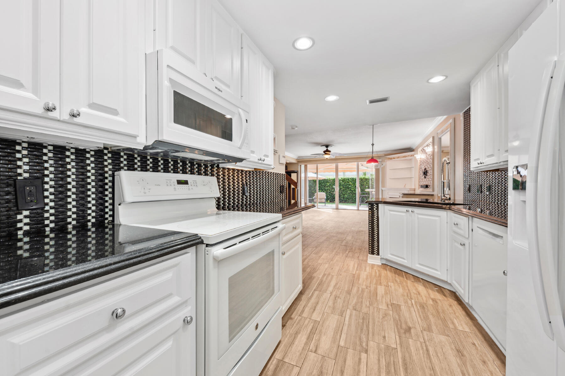 Kitchen featuring white cabinetry, dark countertops, a geometric mosaic tile backsplash, wood-finish flooring, and recessed lighting