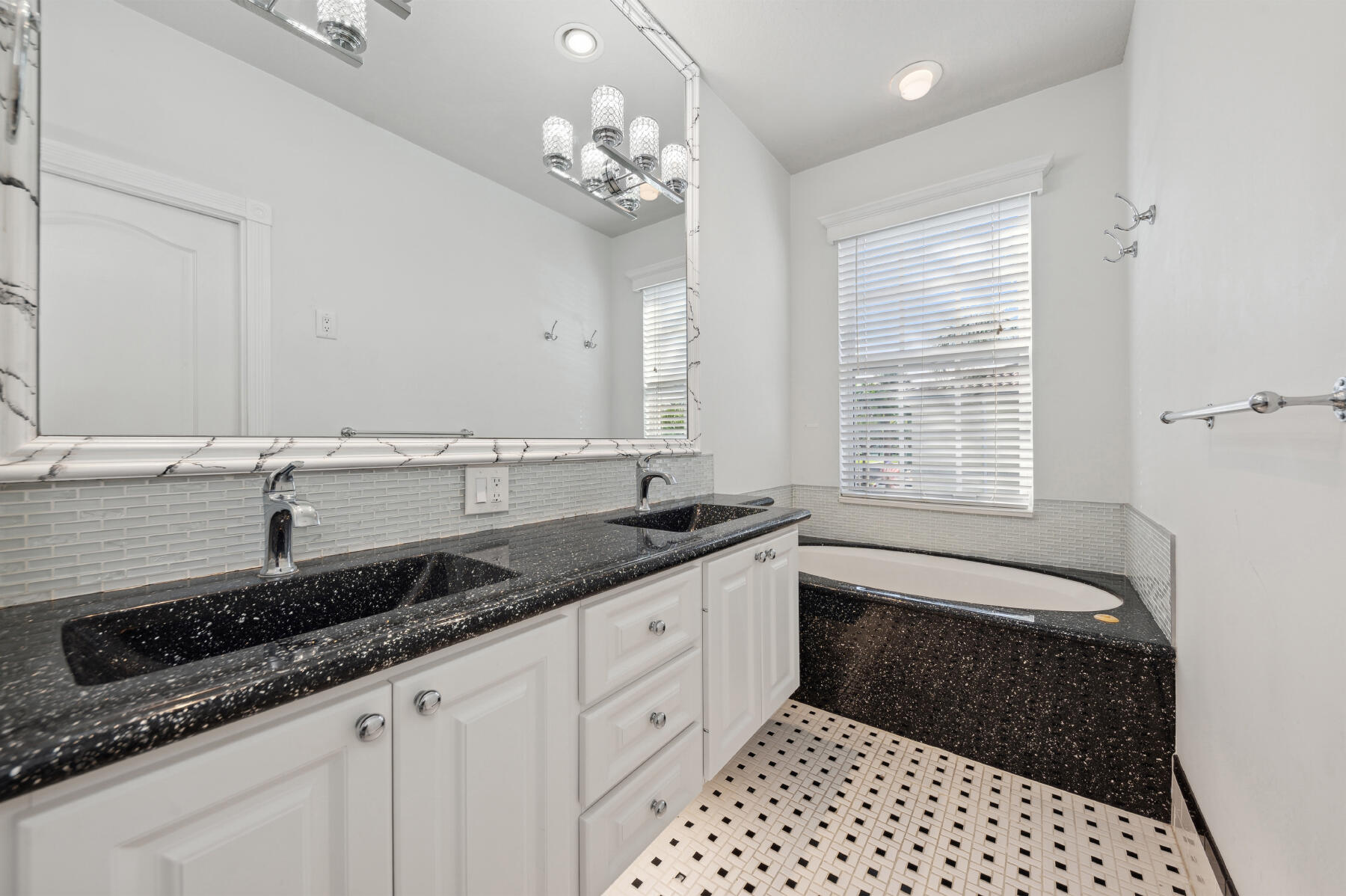 Dual-sink vanity with stone-finish countertops, undermount sinks, white cabinetry, integrated soaking tub, and decorative wall-to-wall mirror with frame detail
