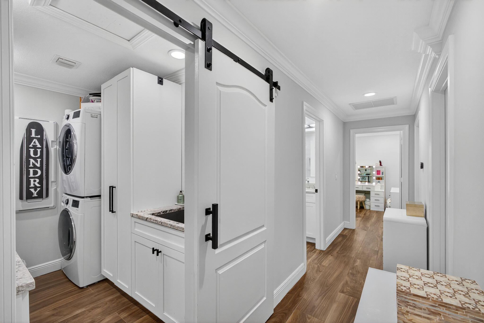 Laundry room featuring a white sliding barn door with matte black hardware, stacked washer and dryer, custom white cabinetry, and wood-finish flooring