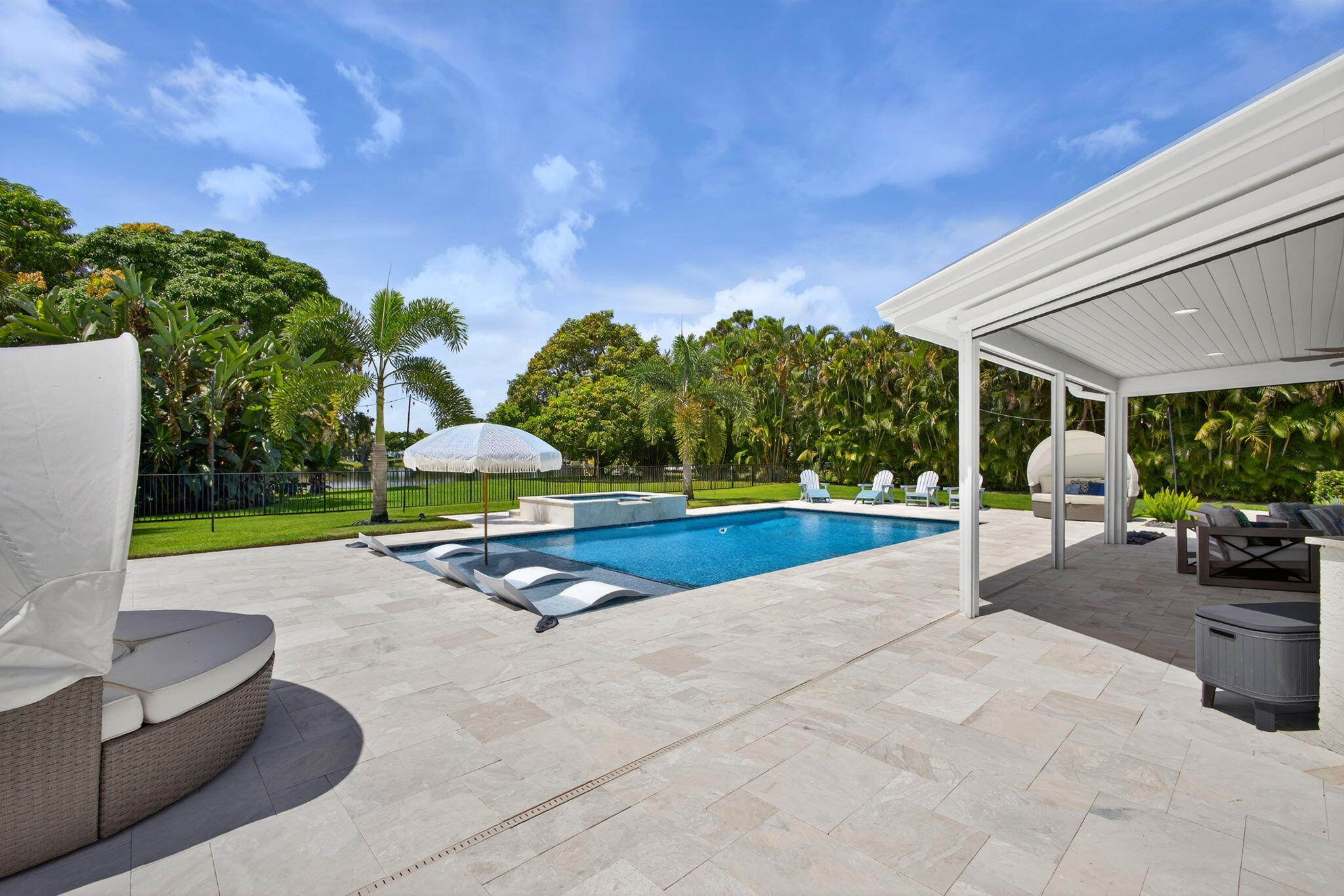 Outdoor living area featuring a covered lanai with a beadboard ceiling, expansive stone paver patio, swimming pool with an integrated spa, and manicured lawn