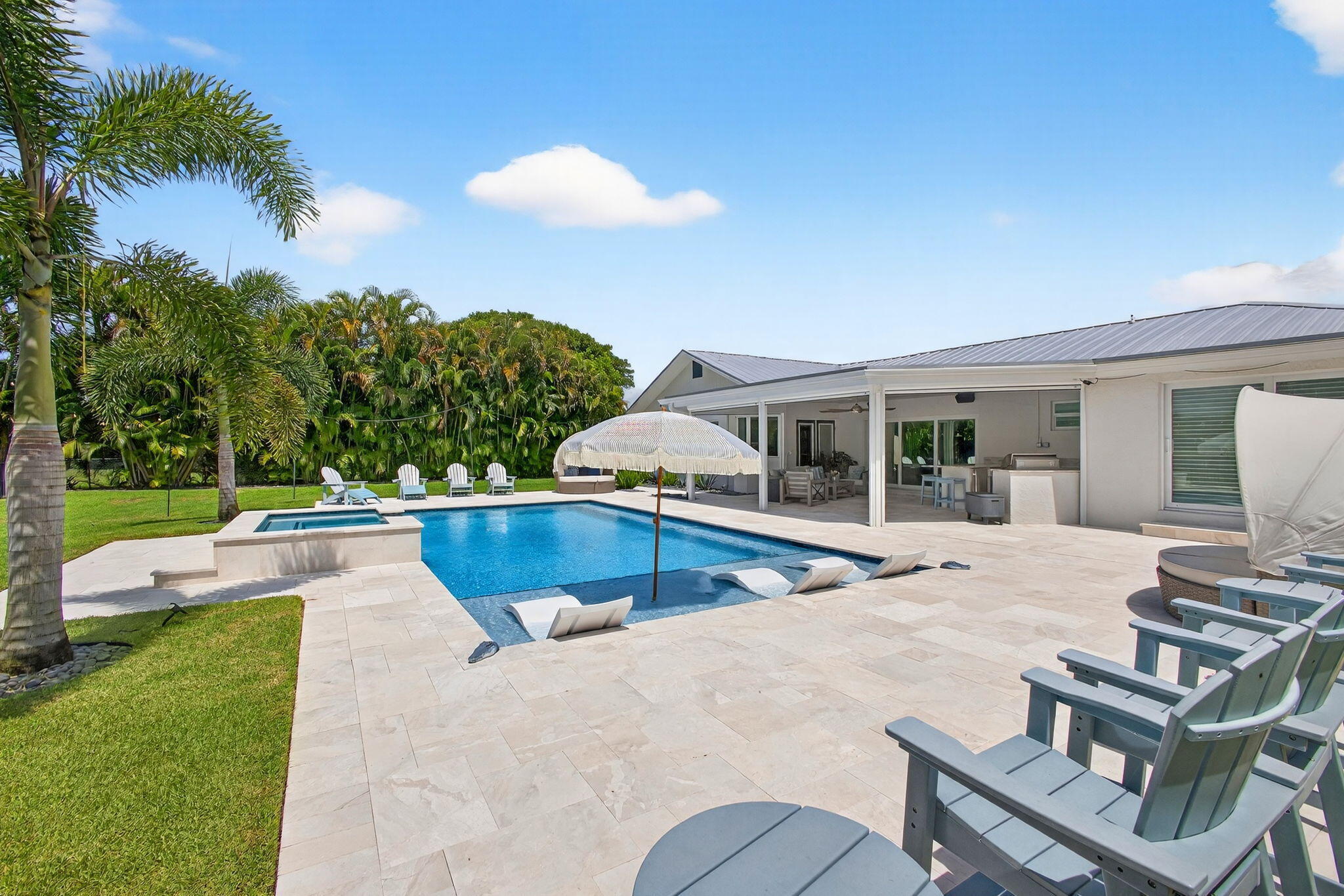 Backyard oasis featuring an in-ground pool with a spillover spa, expansive light-toned stone patio, covered lanai, and manicured lawn