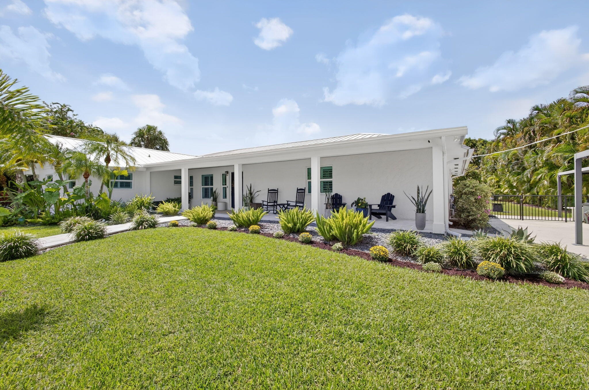 Exterior featuring a covered porch, white stucco finish, metal roof, and landscaped lawn with mature greenery