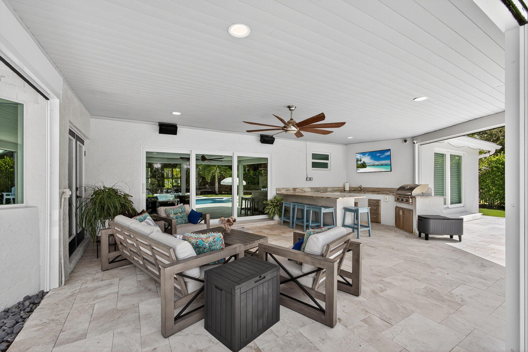 Covered outdoor living space featuring natural stone flooring, tongue-and-groove ceiling, recessed lighting, and a built-in outdoor kitchen with a stainless steel grill