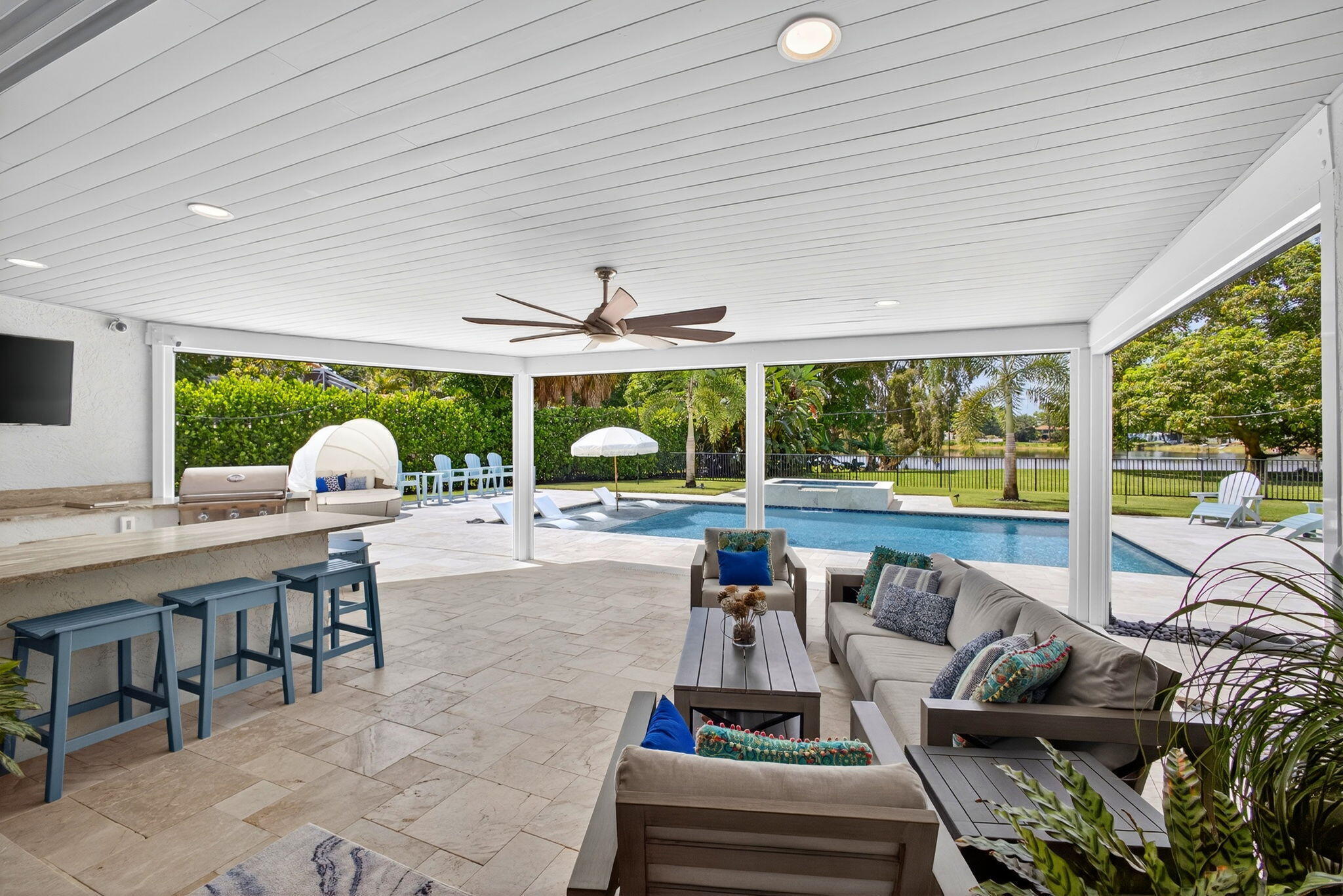 Covered patio featuring a built-in outdoor kitchen with stone countertops, recessed lighting, ceiling fan, and stone paver flooring overlooking an in-ground swimming pool and spa