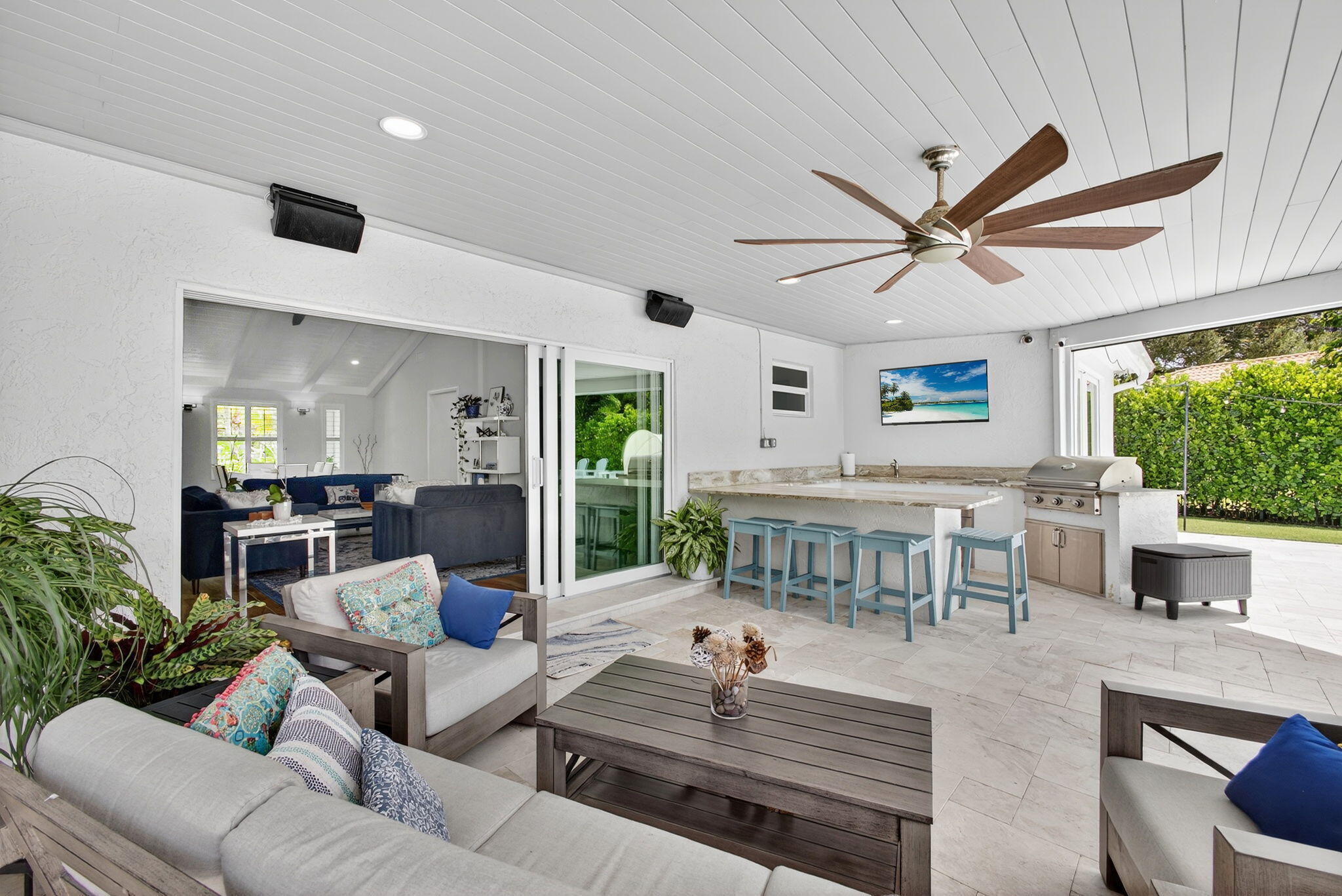Covered patio featuring large-format stone flooring, tongue-and-groove ceiling, multi-blade ceiling fan, and built-in outdoor kitchen with stone countertop and stainless steel grill