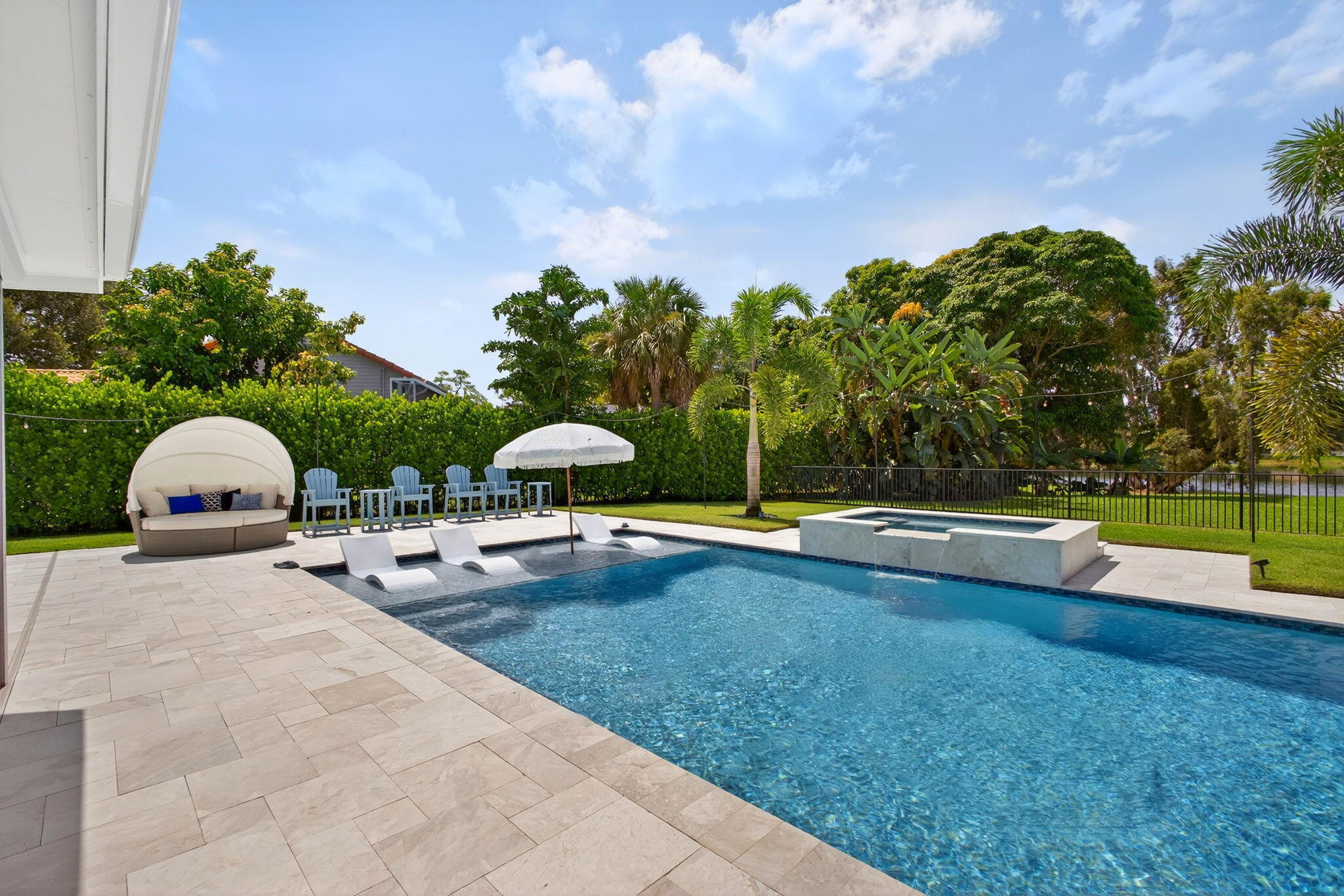 Outdoor space featuring an in-ground pool with a tanning ledge, a raised integrated spa, stone-paver decking, and manicured privacy hedging